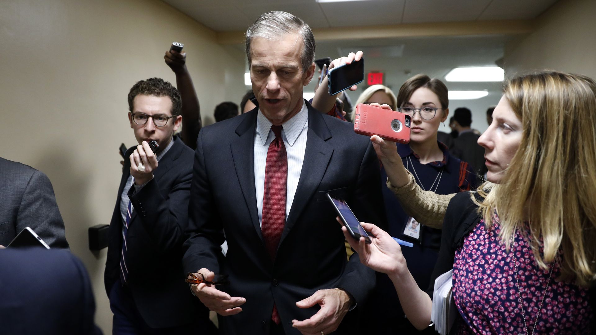Senator John Thune walks in a suit as reporters follow him asking questions