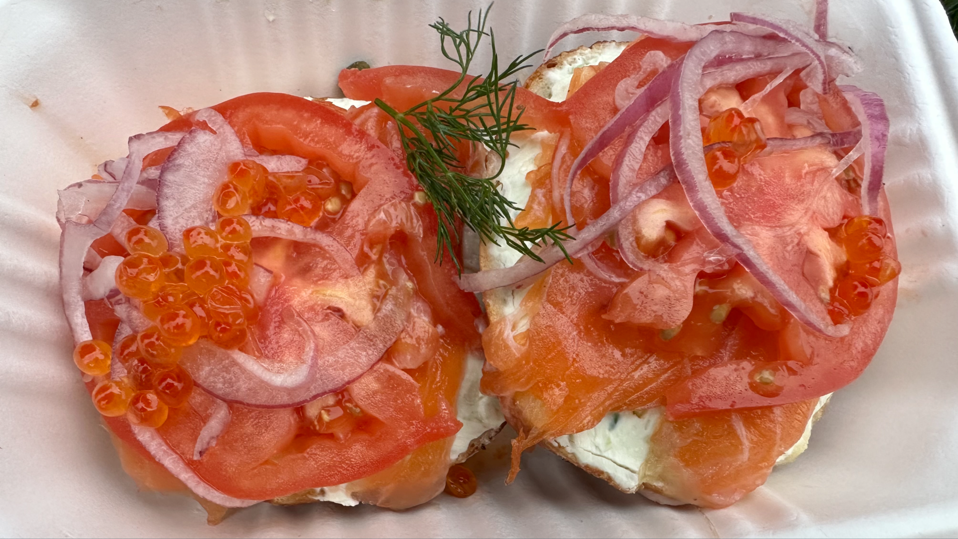 Tomato with roe and salmon on top of a bagel that is served open faced.