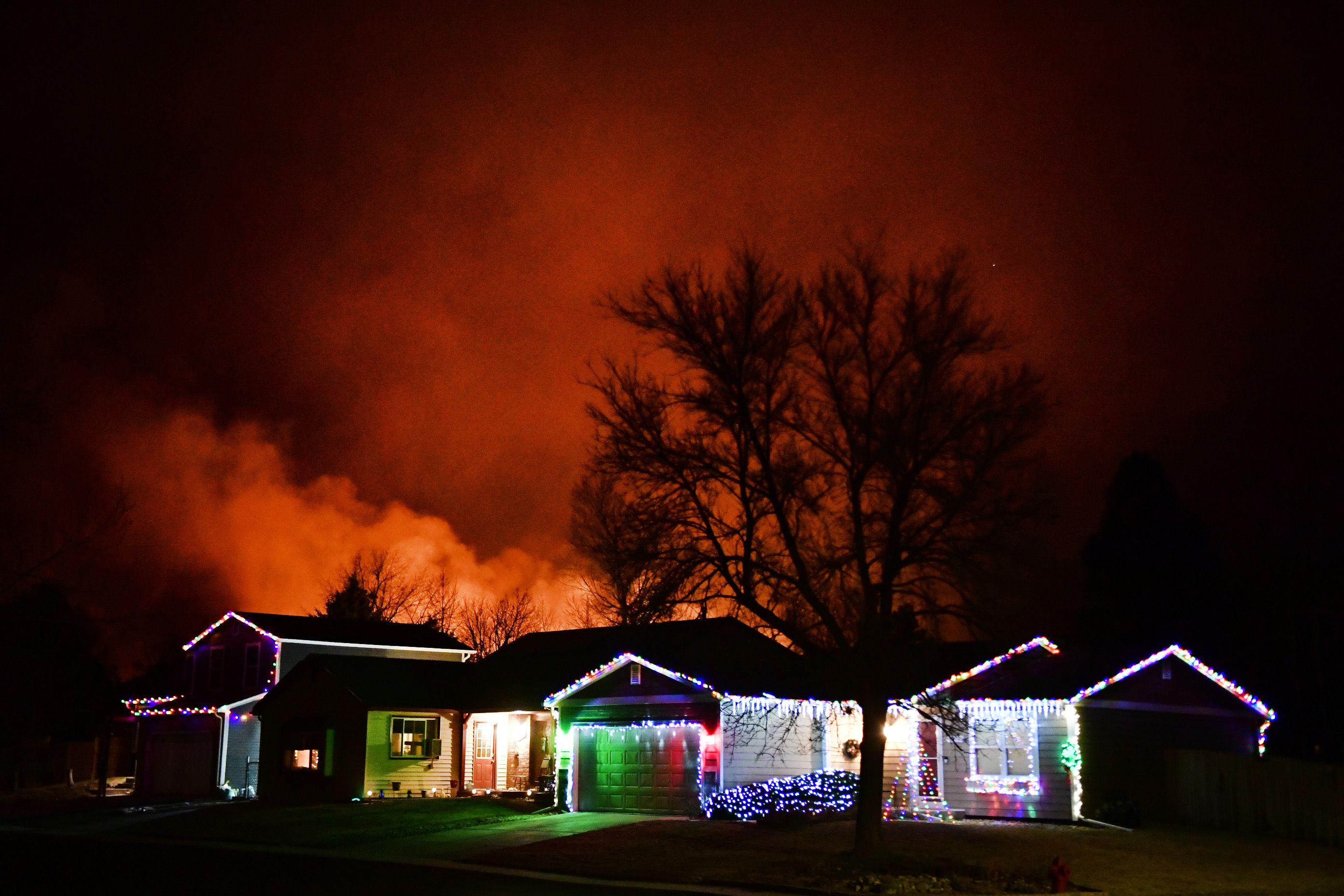 Christmas lights adorn a house as fires rage in the background.