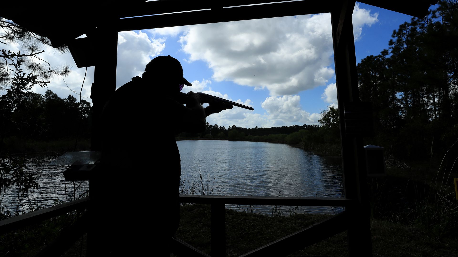 A rifleman in silhouette aims a gun over a lake 