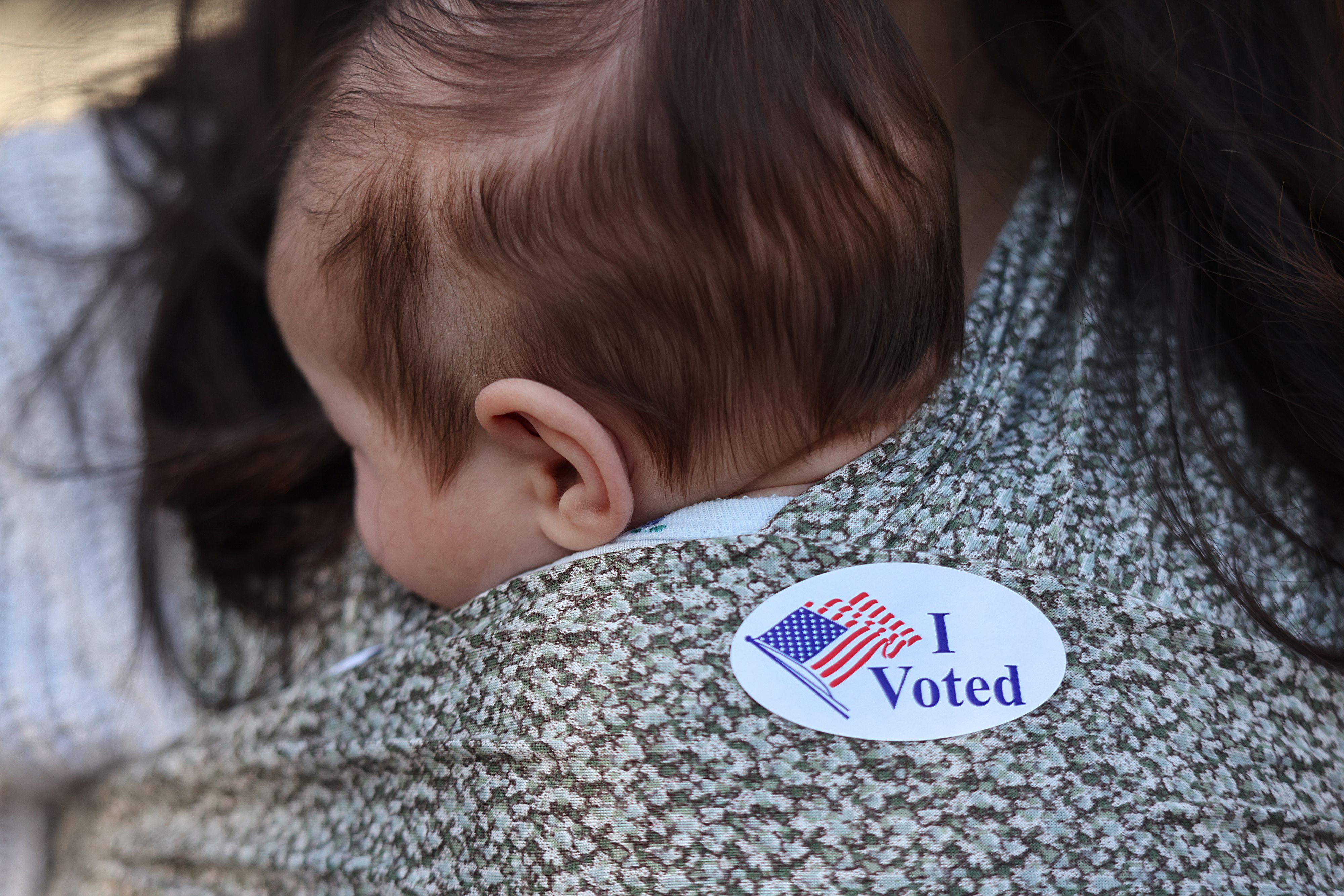 A baby with an "I Voted" sticker on it's blanket. 