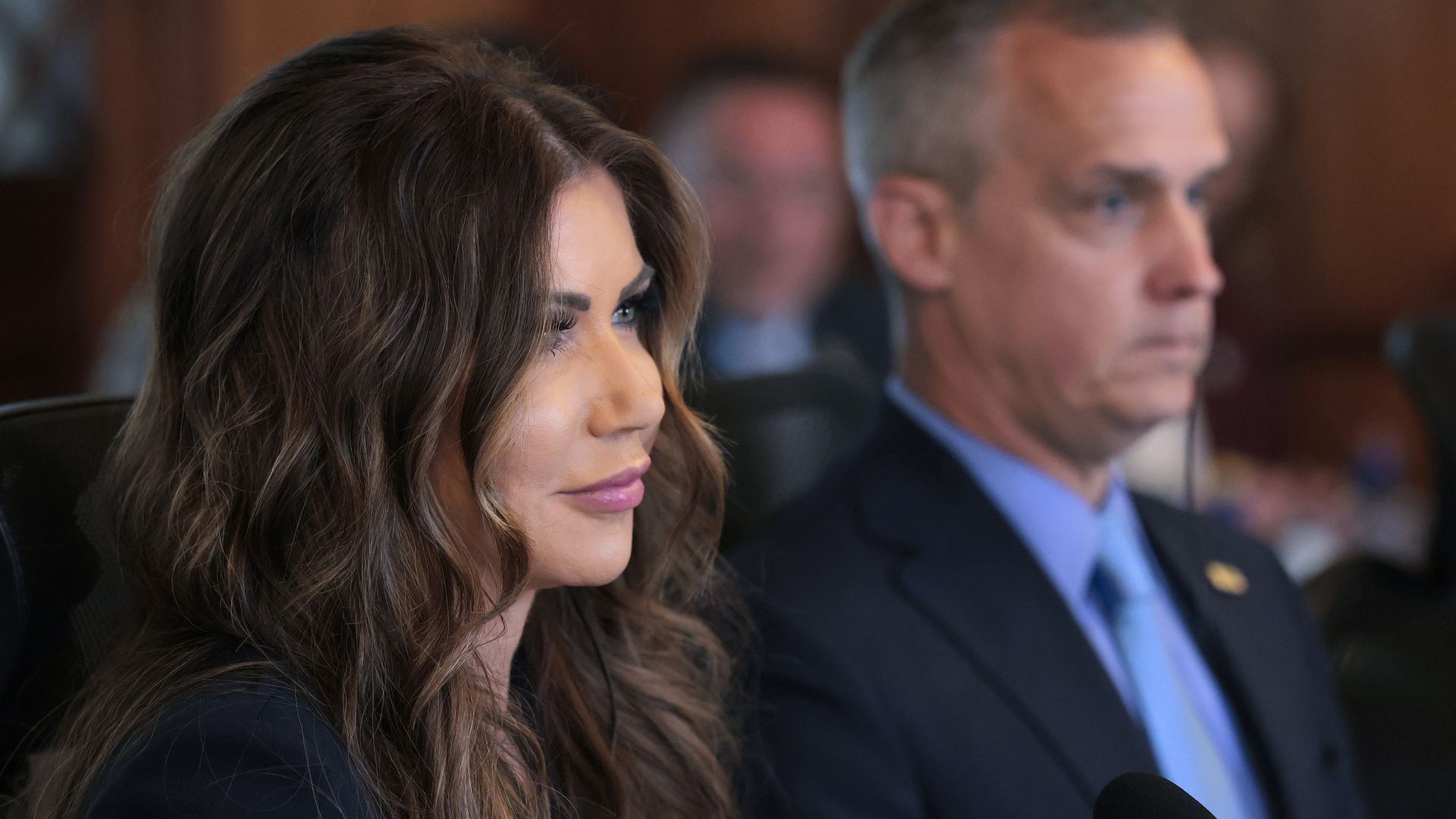 Homeland Security Secretary Kristi Noem in the foreground, and a blurred image of adviser Corey Lewandowski in the background.