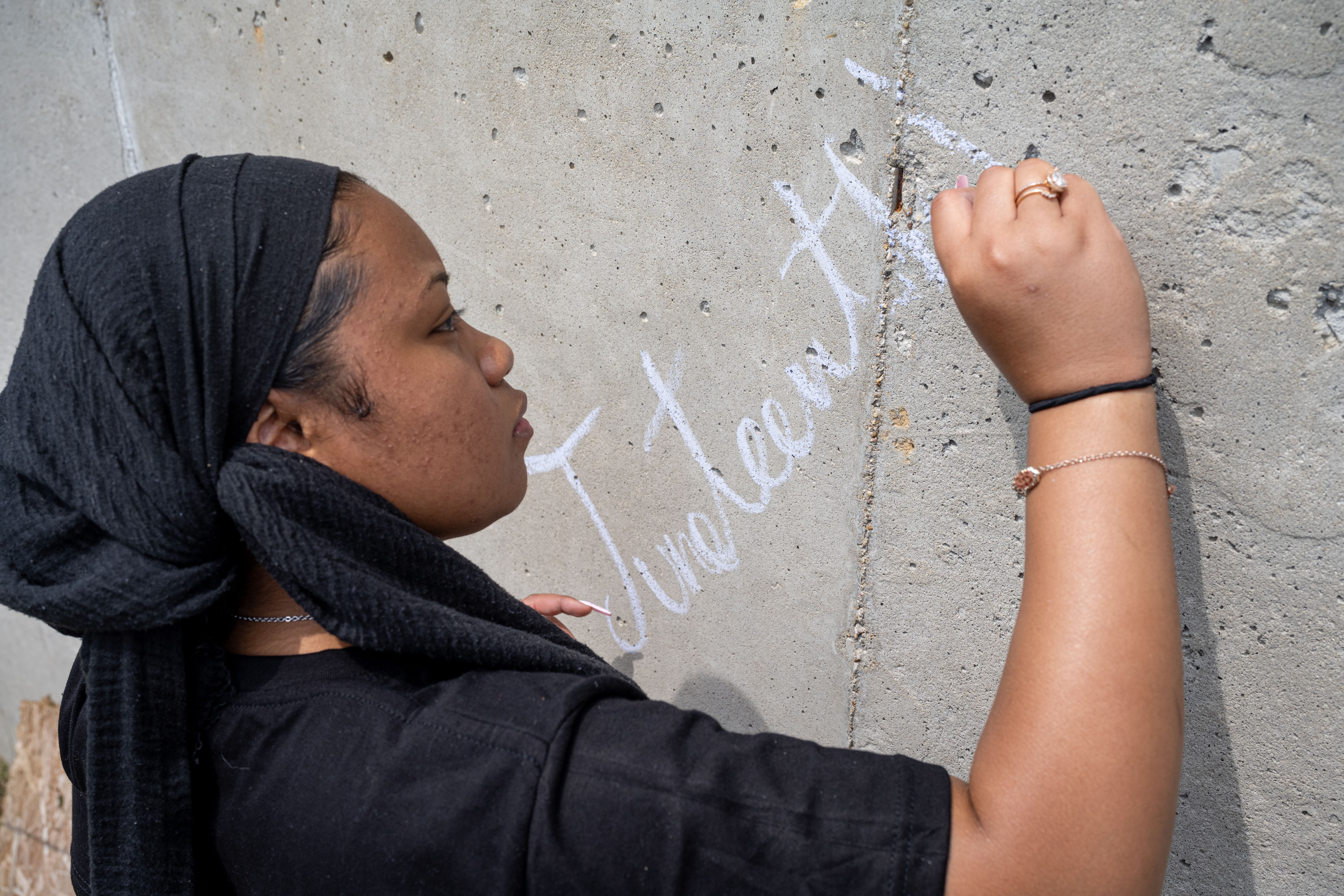 Photo of a young person writing "Juneteenth" on a wall with chalk