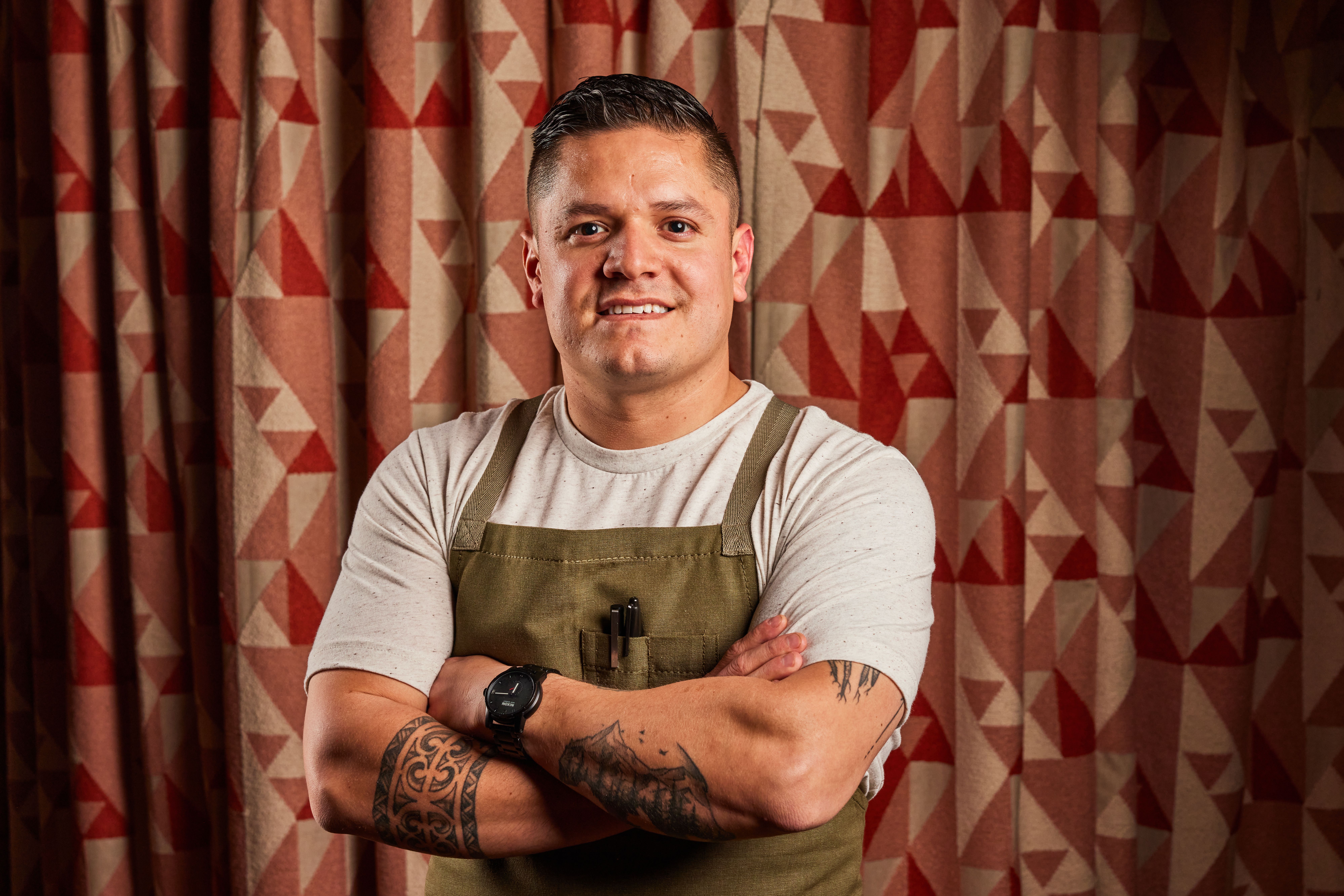 A man in a light shirt and a dark green apron poses for a photo. 