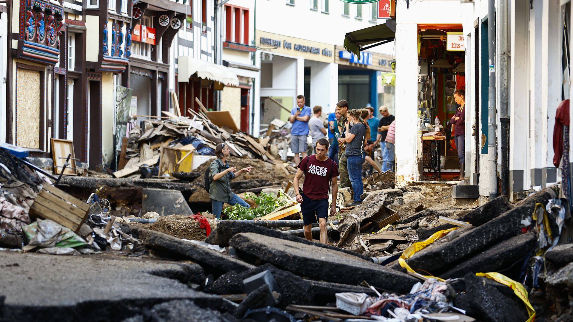 Street filled with rubble with people walking in between closed storefronts.