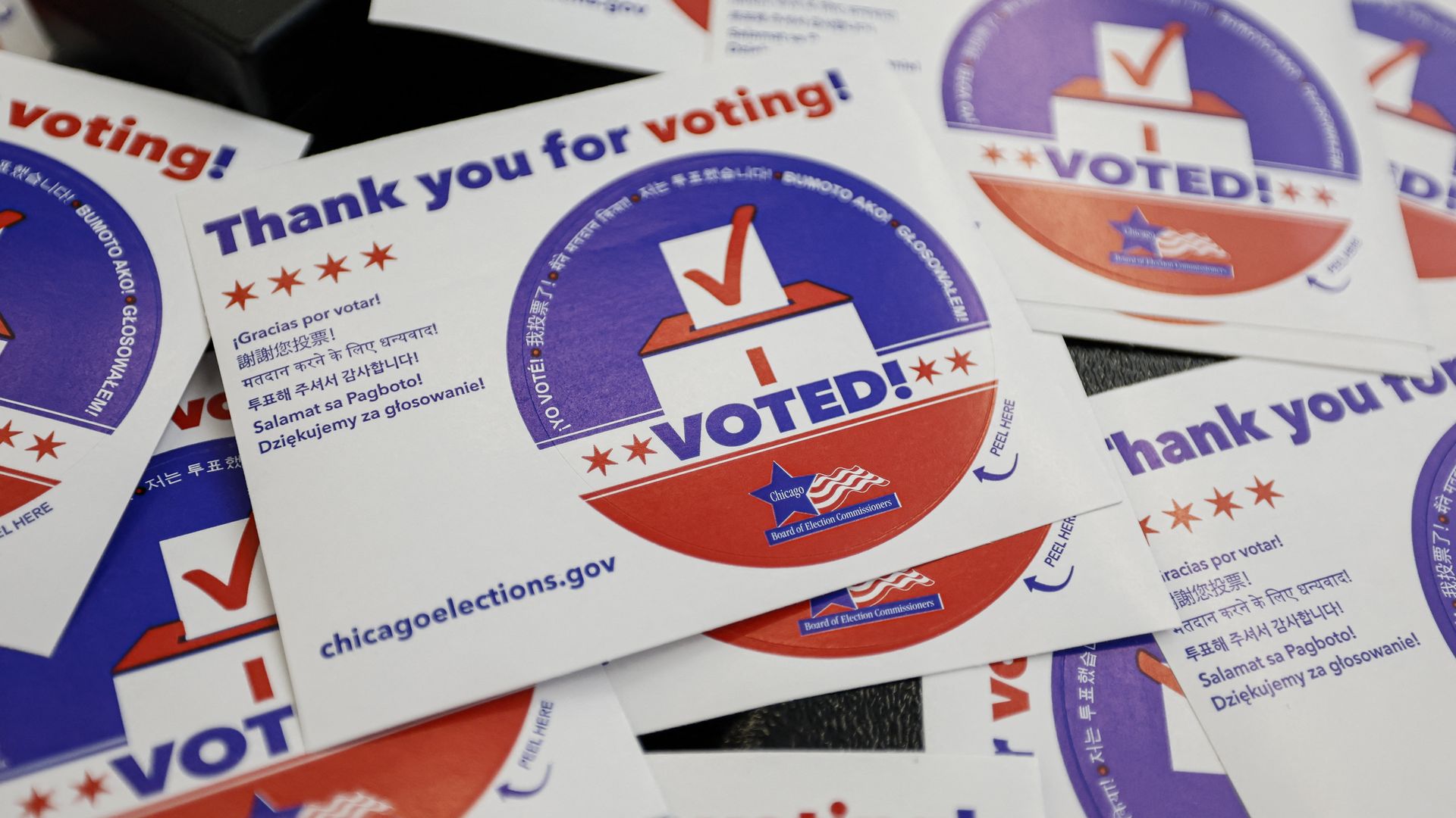 Pile of I VOTED! stickers featuring a purple circular seal with a red ballot box and checkmark, plus the phrase Thank you for voting! in multiple languages.