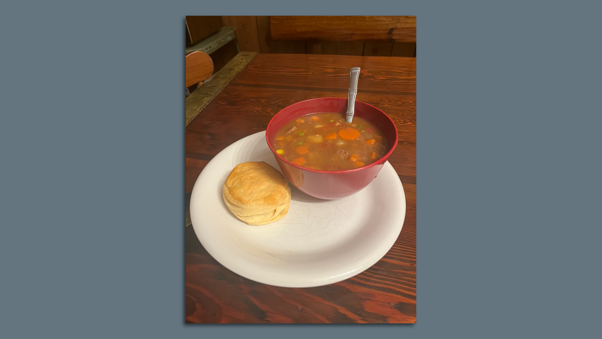A bowl of soup sitting on a plate next to a biscuit.