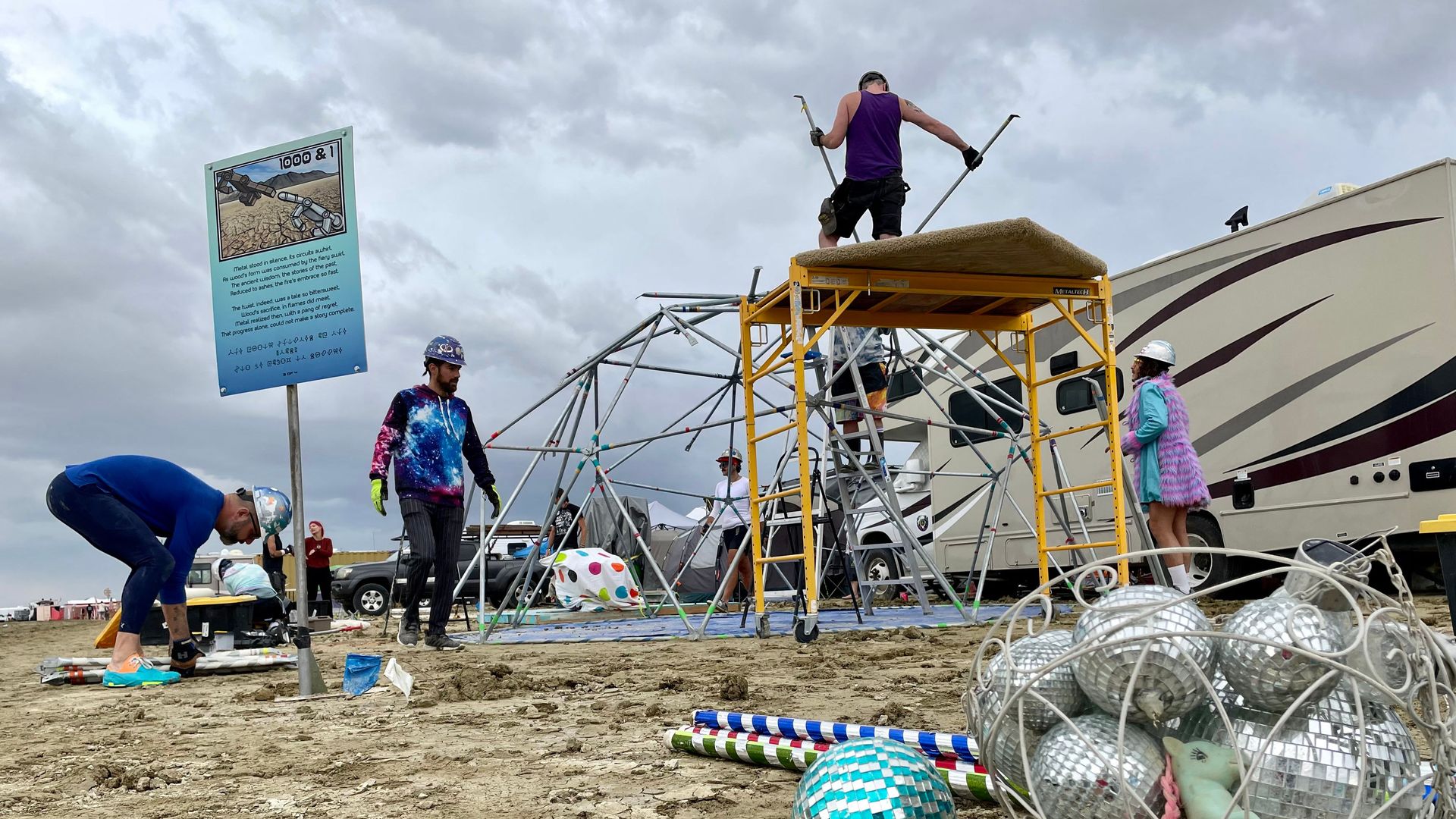People take down a structure at Burning Man. Disco balls are in the foreground on the desert floor. 