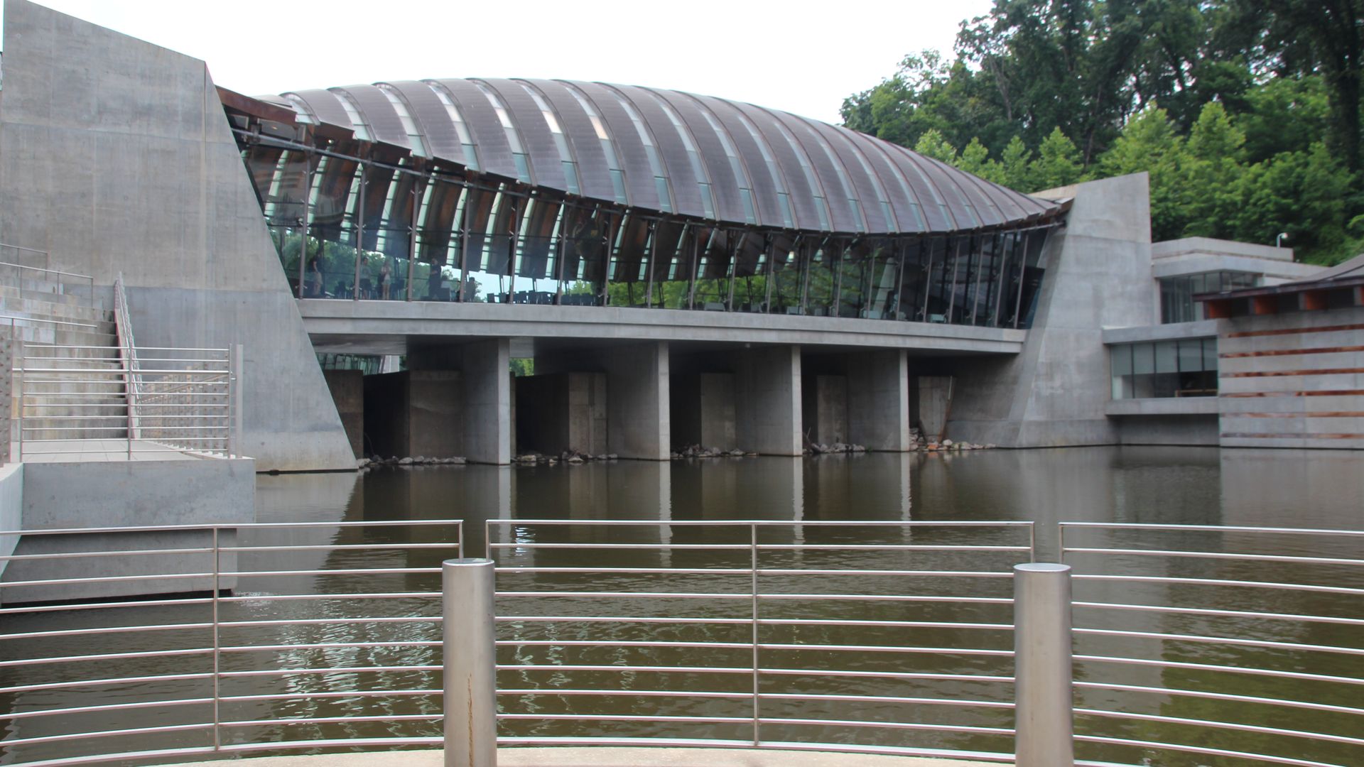 A view of the outside of the Crystal Bridges art museum, surrounded by a body of water.