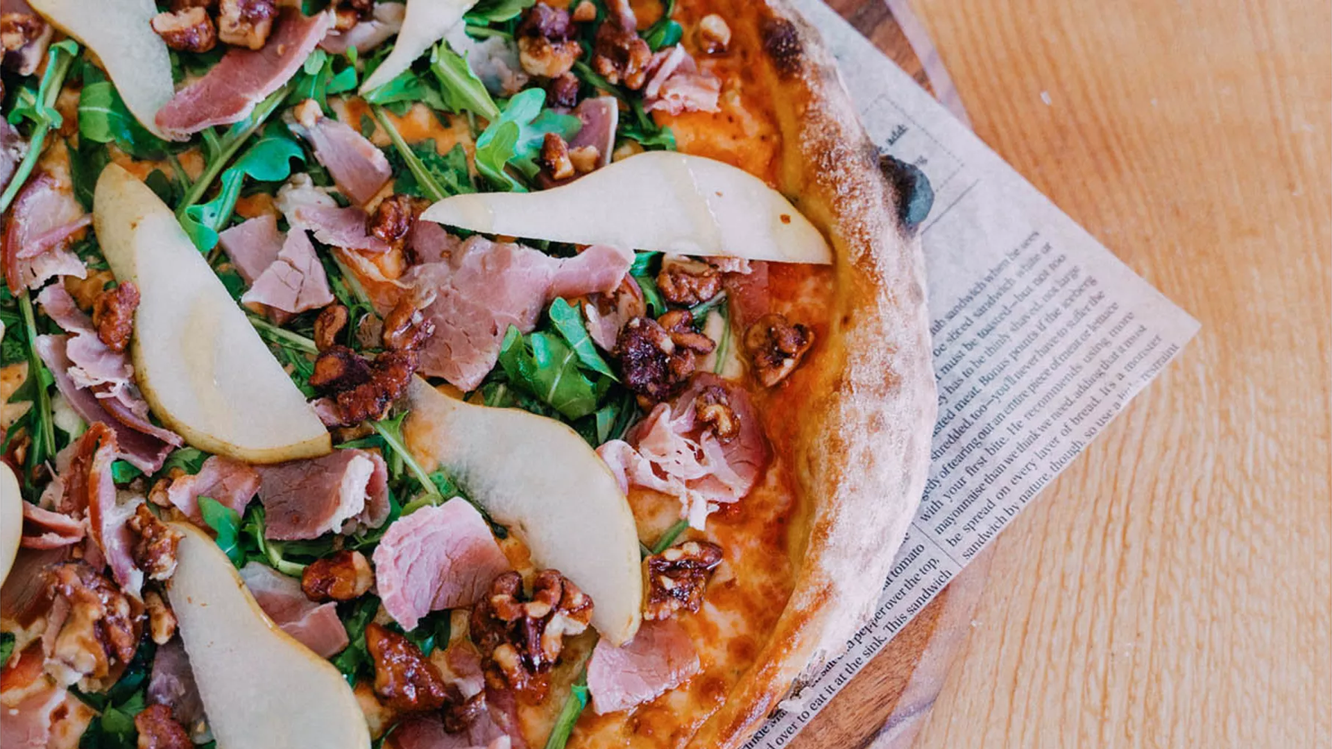 A large pizza with meat, greens and pears on top.