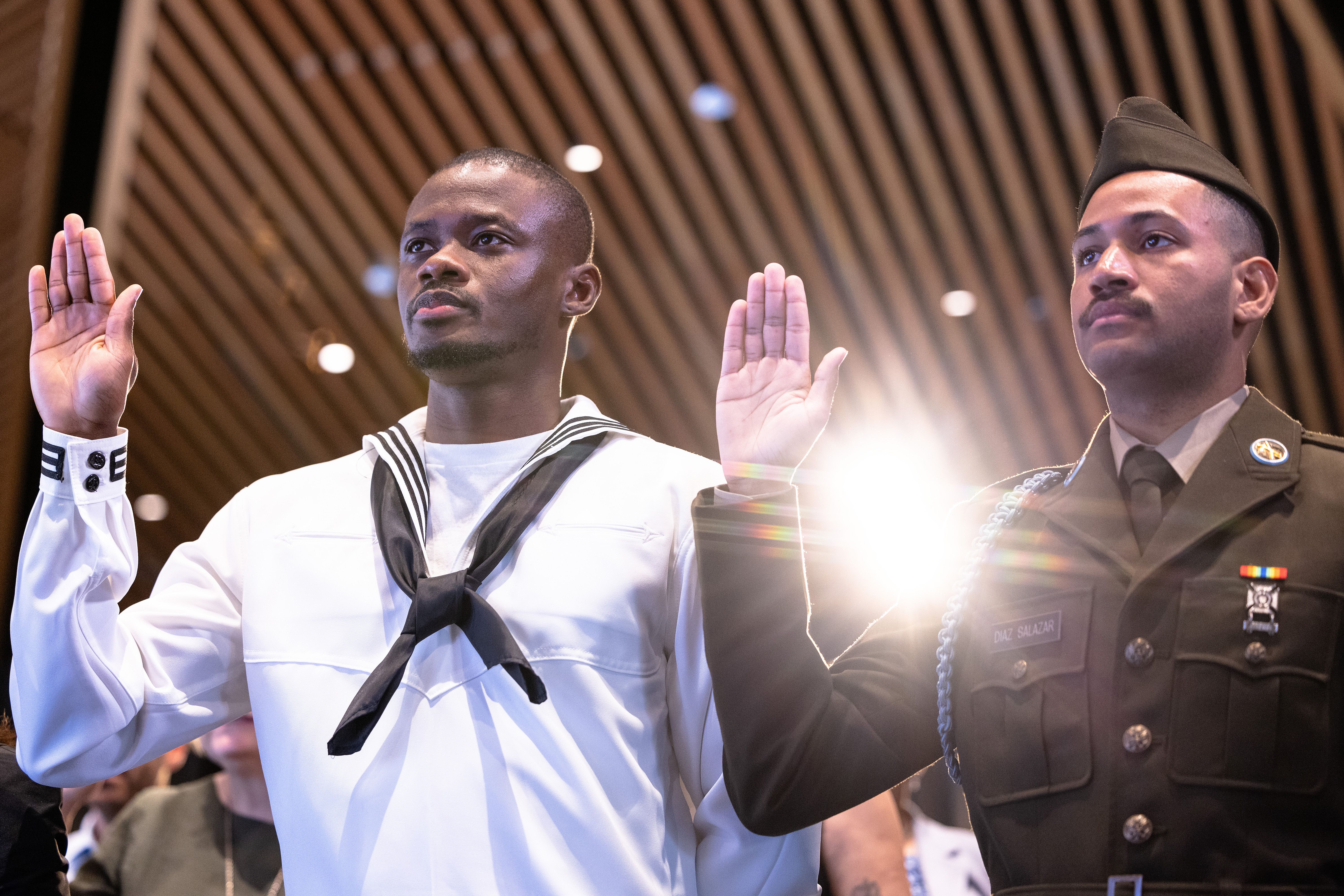 : Oscar Innocent, who is originally from Nigeria, and Cristian Diaz, originally from Dominican Republic, raise their hands as they take the Oath of Allegiance during a Naturalization Ceremony at the Stavros Niarchos Foundation Library