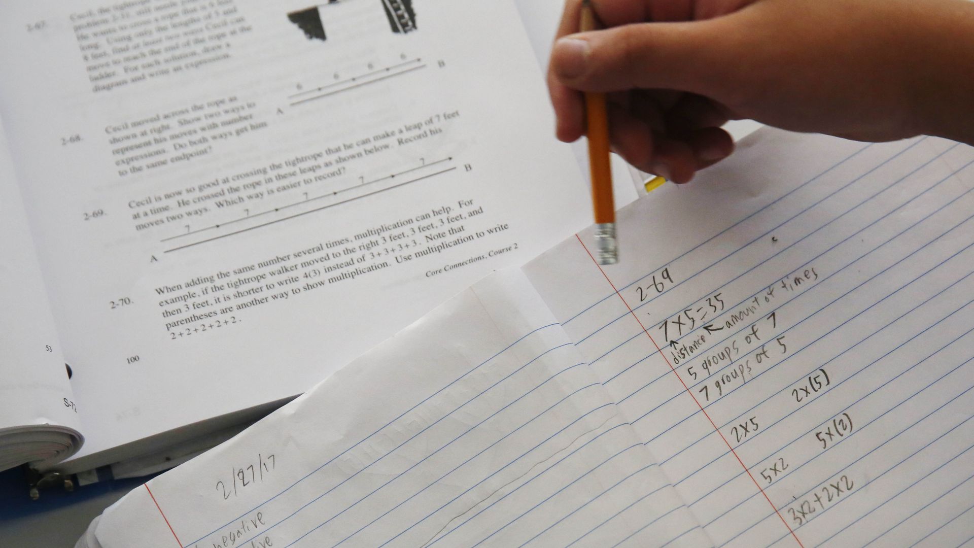 Photo of a hand holding a pencil over a notebook filled with written math equations