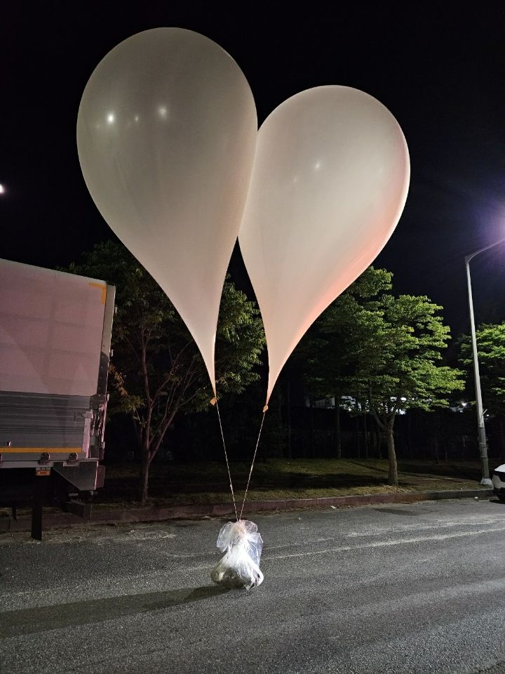 Two white balloons carry a bag of trash. 