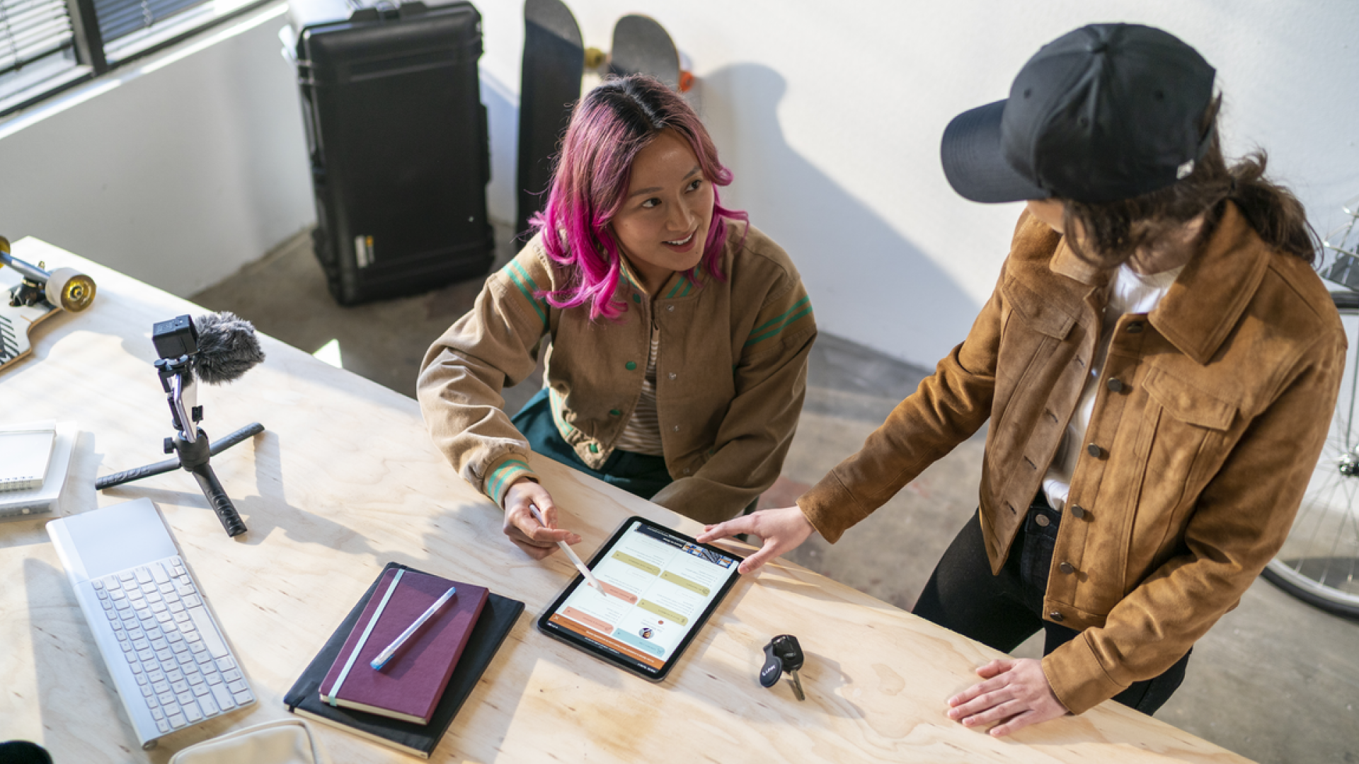 Two women working at a desk, looking at an ipad.