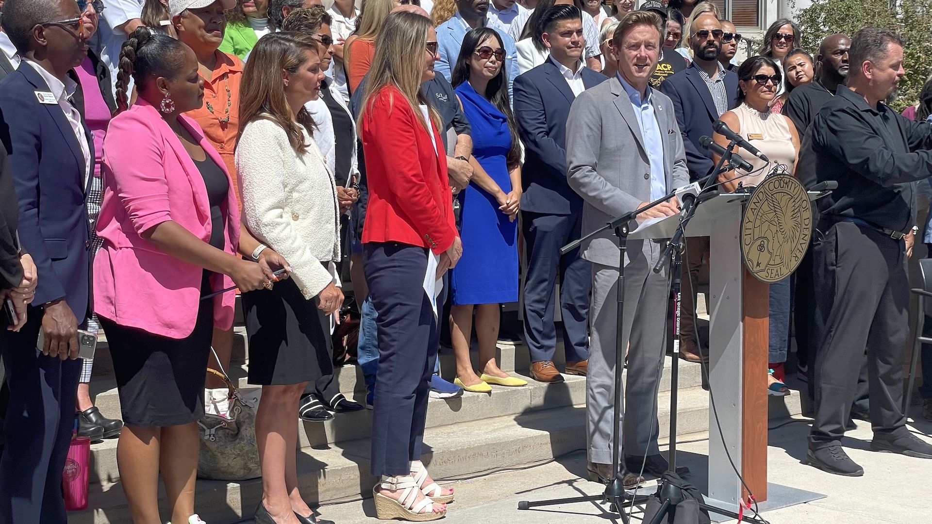 A man in a suit speaks while a large crowd stands behind him.