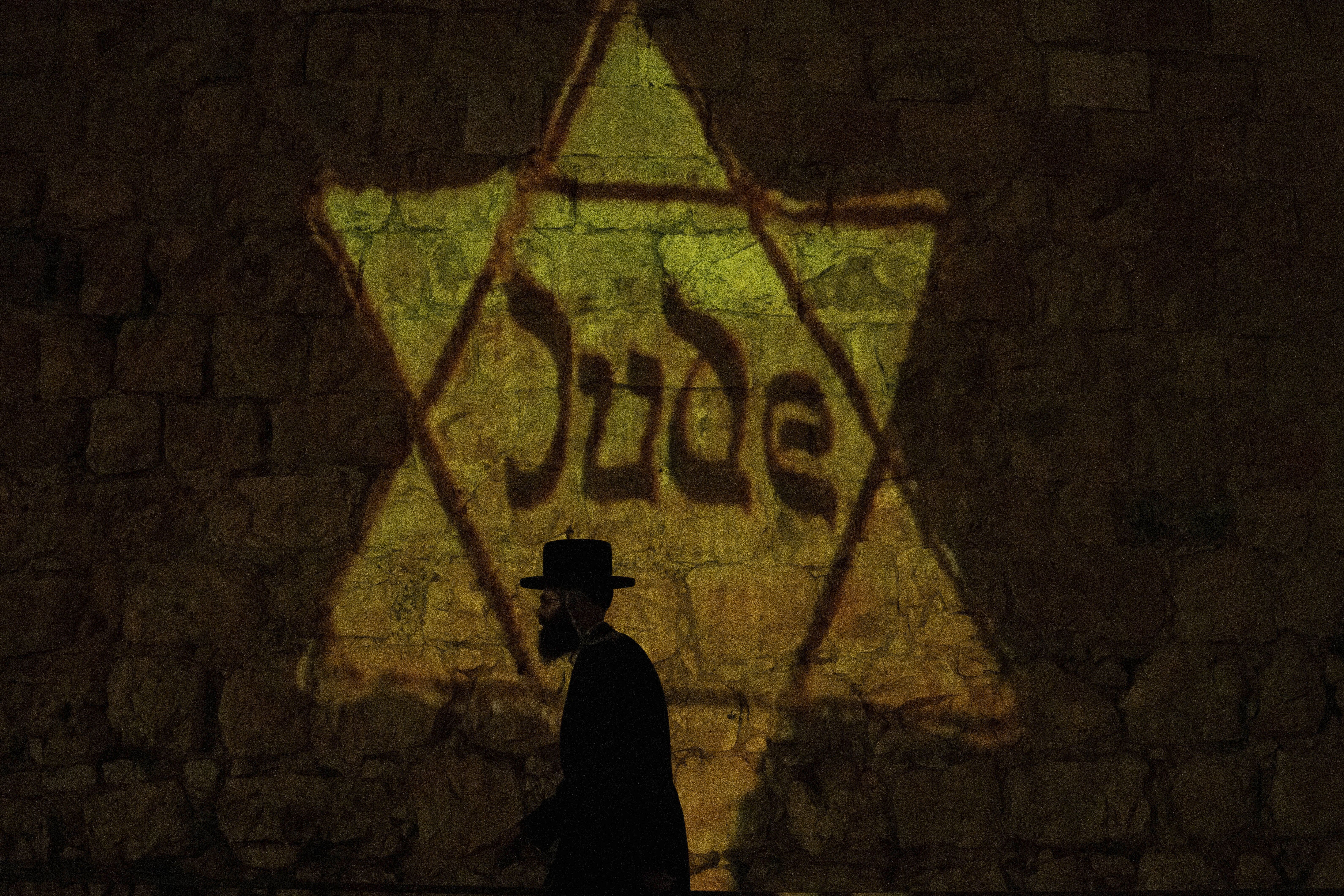 An ultra-Orthodox Jewish man walks by an image of a yellow Star of David that reads "Jude," or Jew in German, resembling the one Jews were forced to wear in Nazi Germany, is projected on the walls of Jerusalem's Old City on the eve of annual Holocaust Remembrance Day, Sunday, May 5, 2024. 