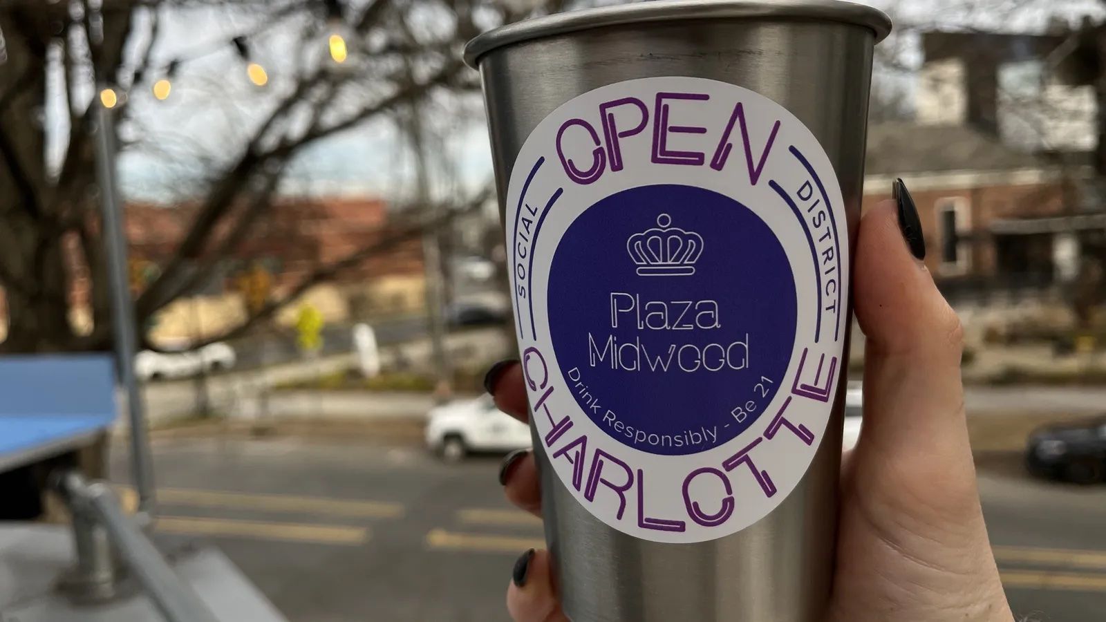 hand holding cup with sticker that reads "plaza midwood social district" 