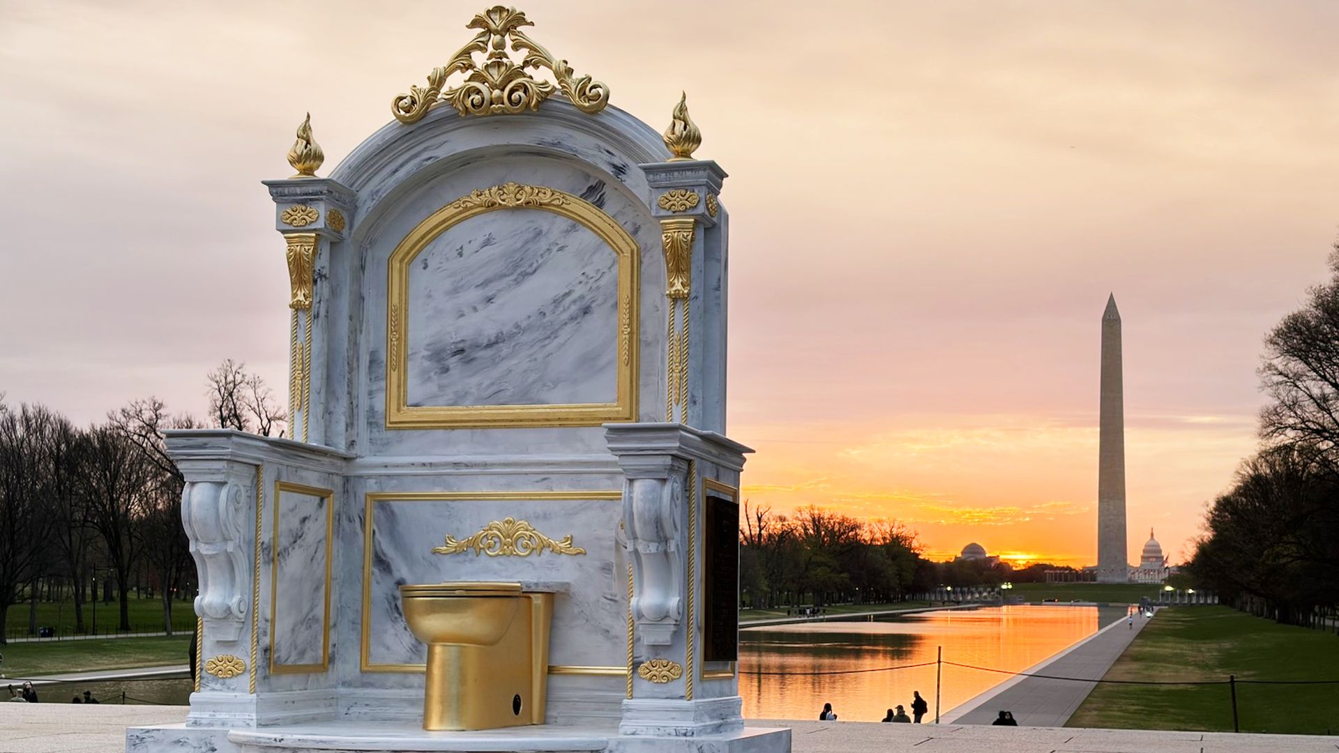 An ornate marble monument with gold trim and a gold basin sits in the foreground; sunset glows over the reflecting pool, with the Washington Monument visible in the distance and bare trees along the banks.