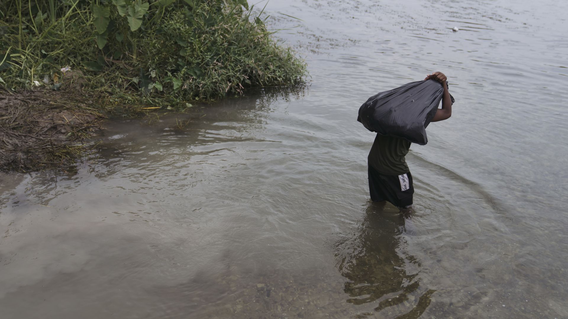Photo of a Haitian migrant holding a bag over their back as they cross a river by foot