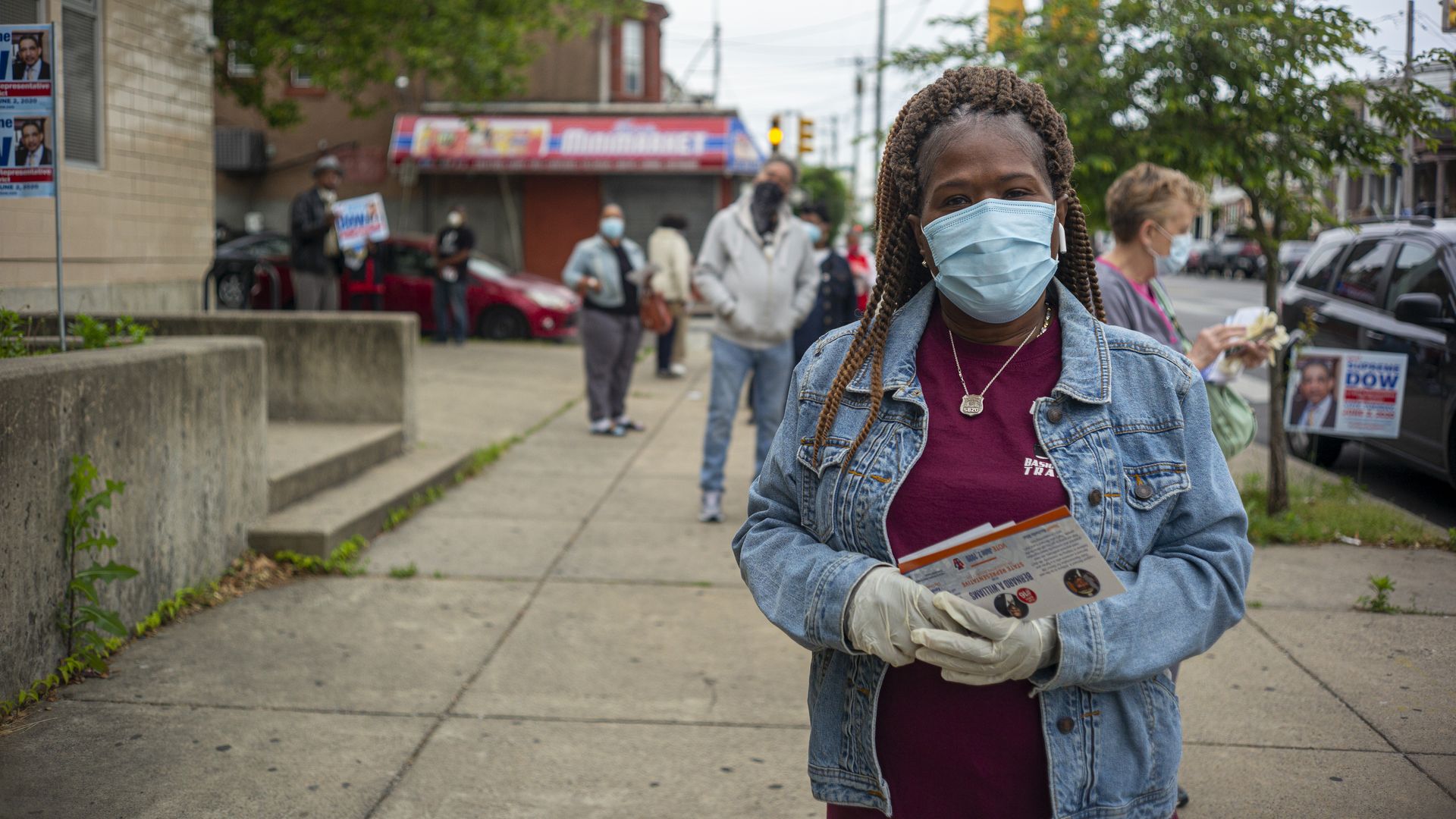 A woman stands in line outside while wearing a face mask, with several people lined up behind her