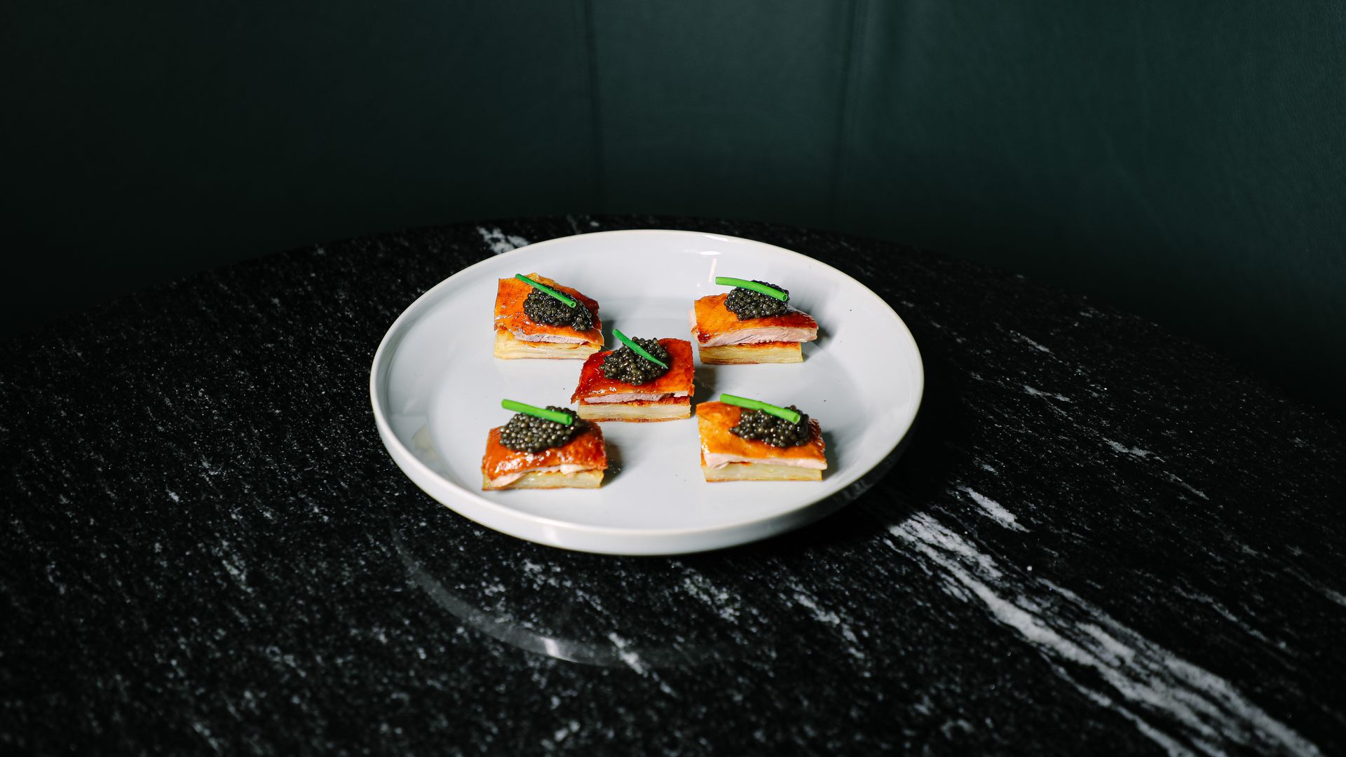 Five pieces of peking duck topped with caviar on a black marble table