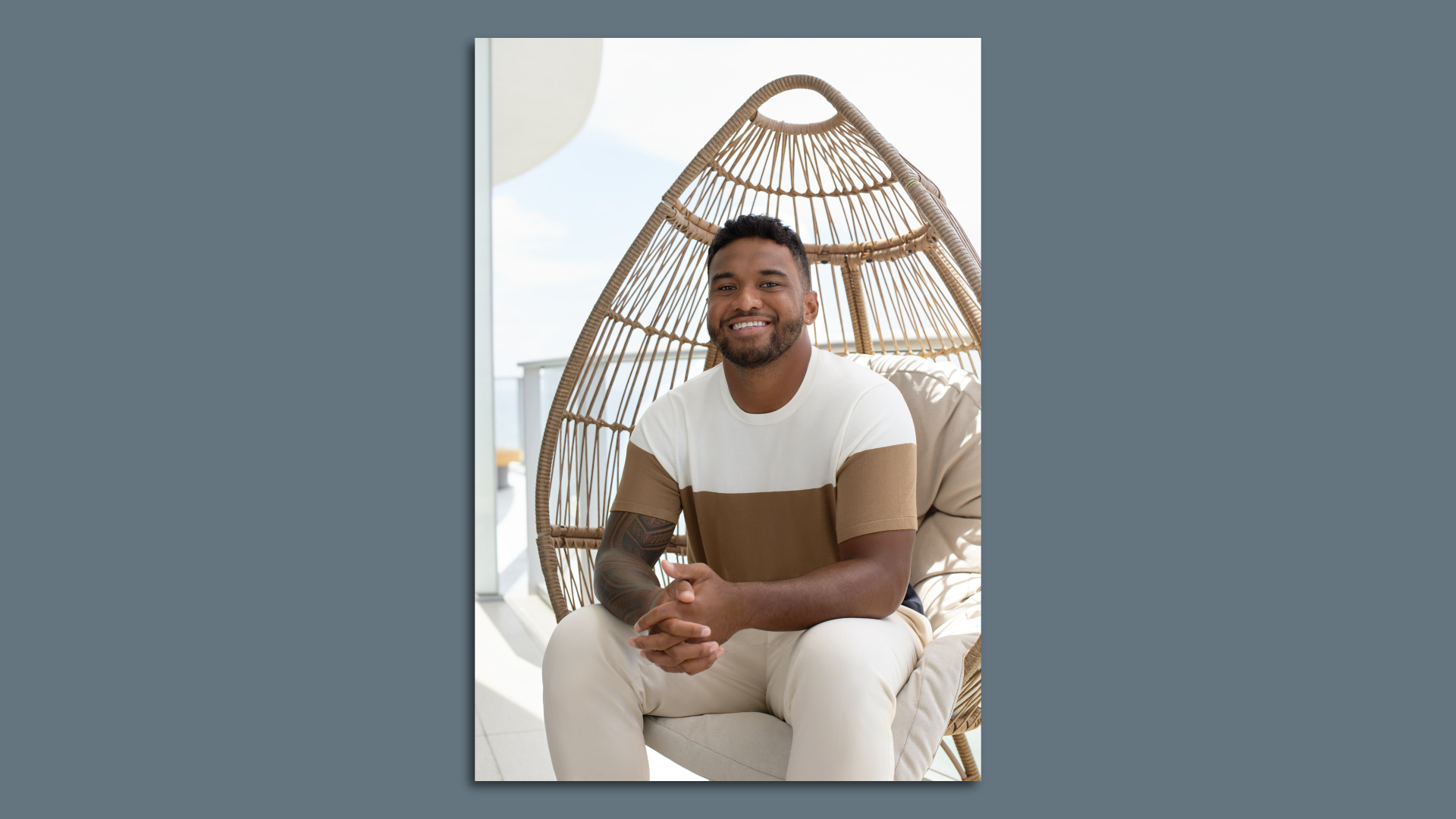 A man sits in a wicker chair with his hands clasped in front of him 