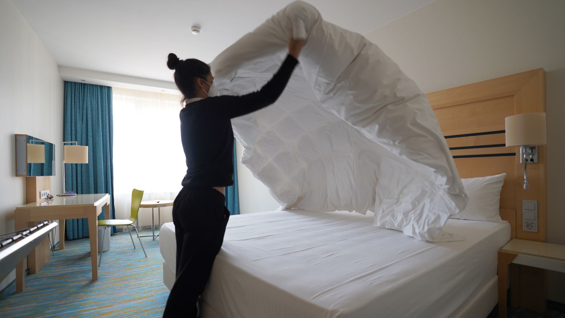 A hotel housekeeper puts a sheet on a bed