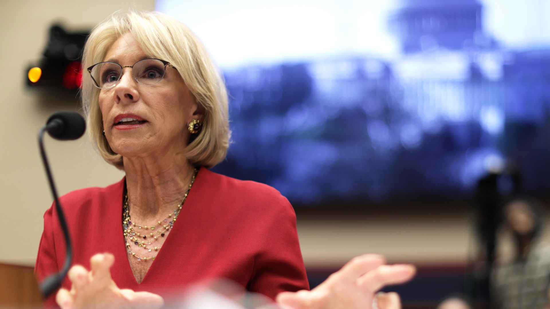 Photo of Betsy DeVos speaking into a mic while gesturing