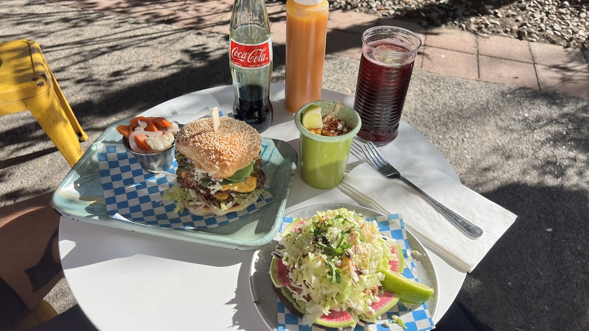 A photo of plates on a white table with a burger and a tostata.