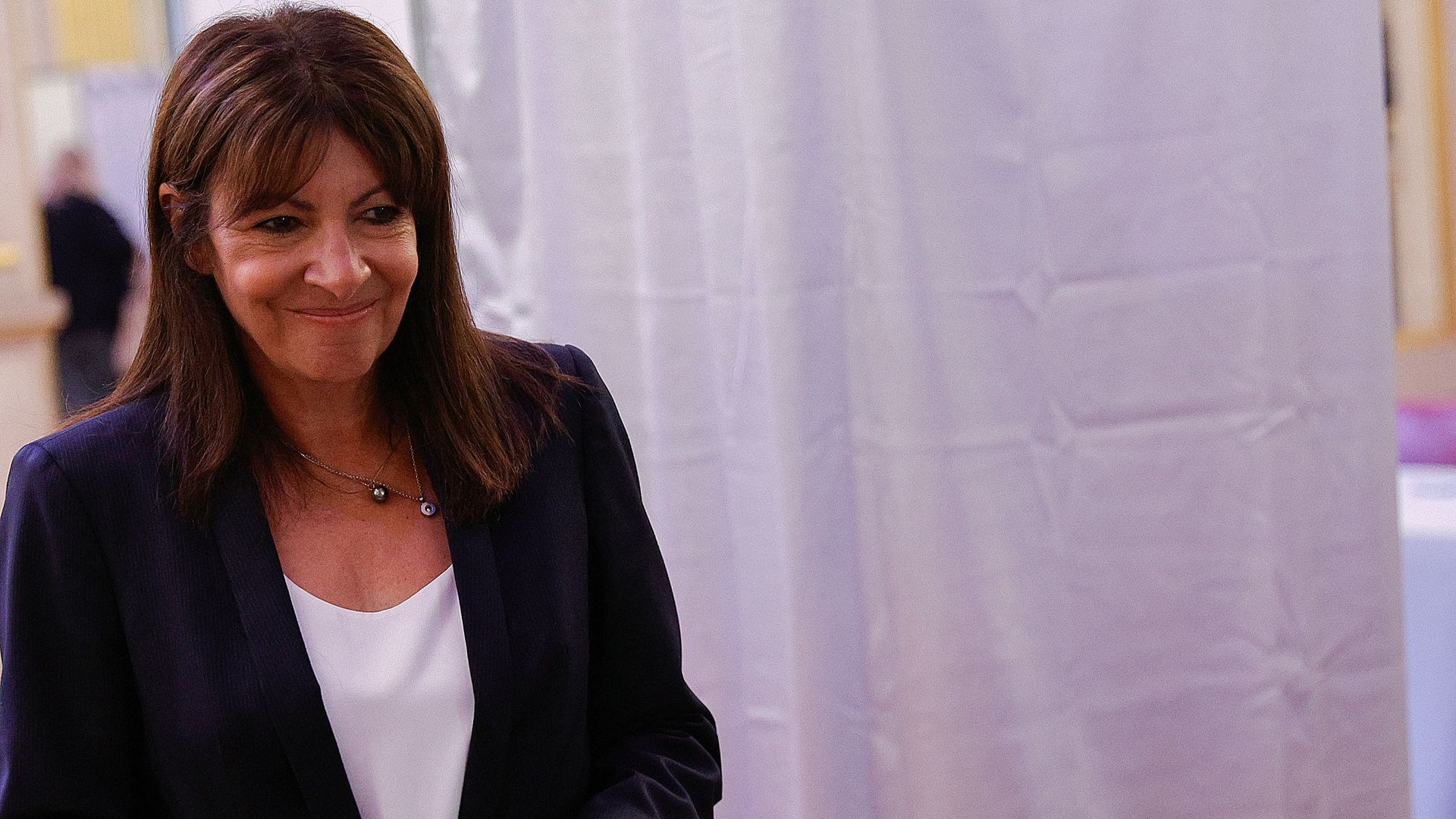 Anne Hidalgo wearing a white shirt and dark blazer holds a ballot 