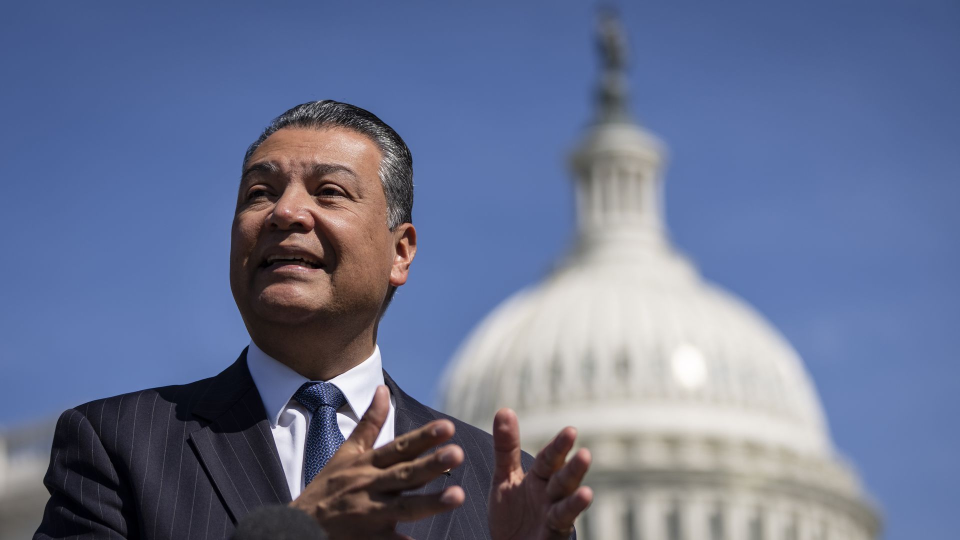 Sen. Alex Padilla stands outside with the U.S. Capitol building blurred behind him 