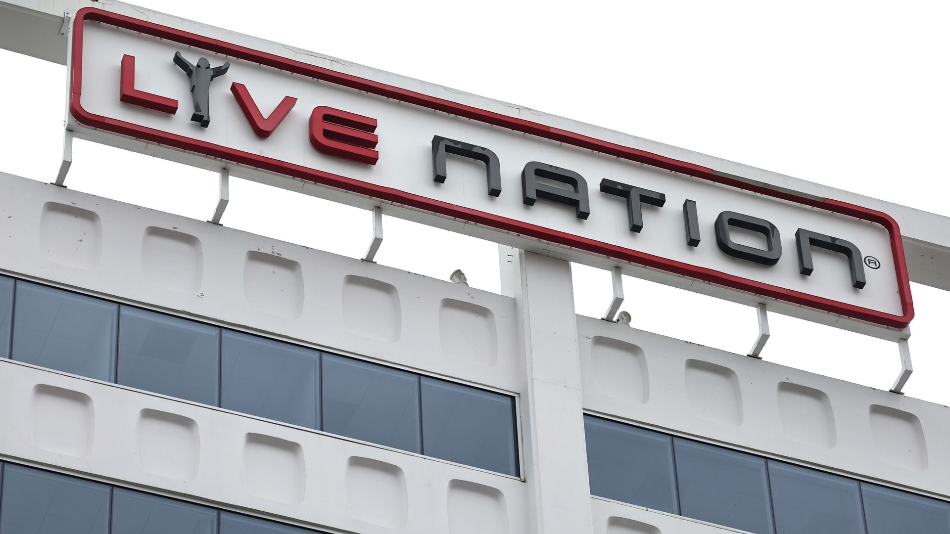 Close-up of a building facade with a white and red sign reading "Live Nation" in black and red letters, featuring a stylized figure in the letter L, above blue-tinted windows.