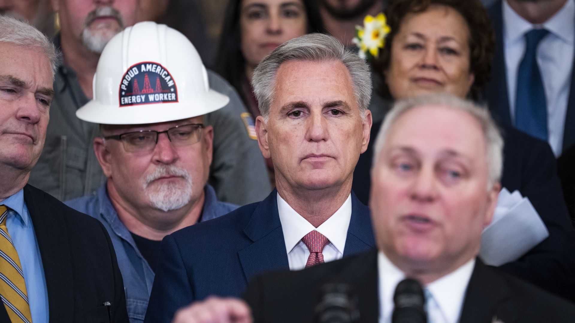 House Speaker Kevin McCarthy, wearing a blue suit, white shirt and pink tie, looks on as Majority Leader Steve Scalise speaks at a press conference.