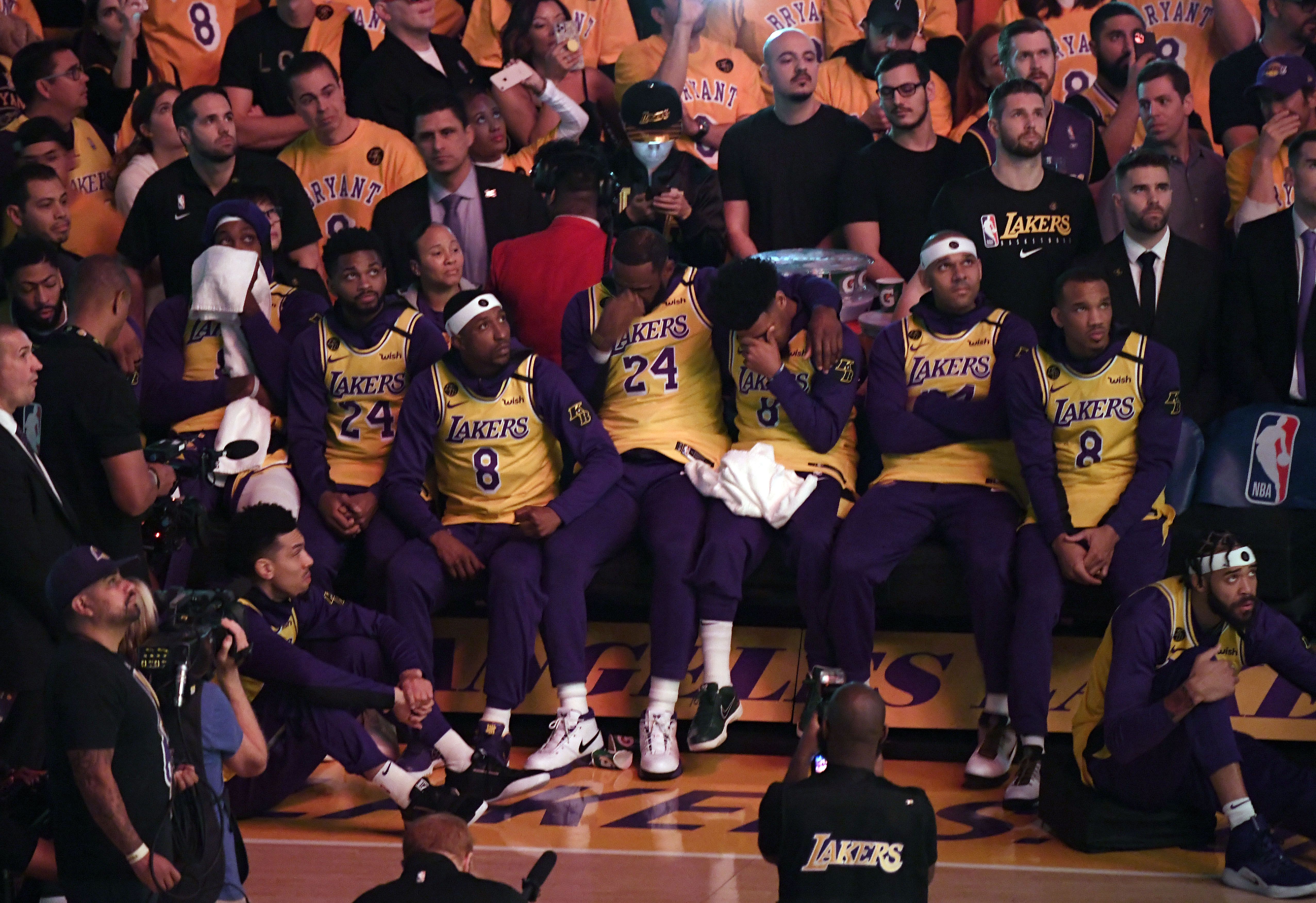 In this image, the Lakers sit next to each other, offering emotional support during the pregame ceremony, sitting courtside and wearing Kobe jerseys 