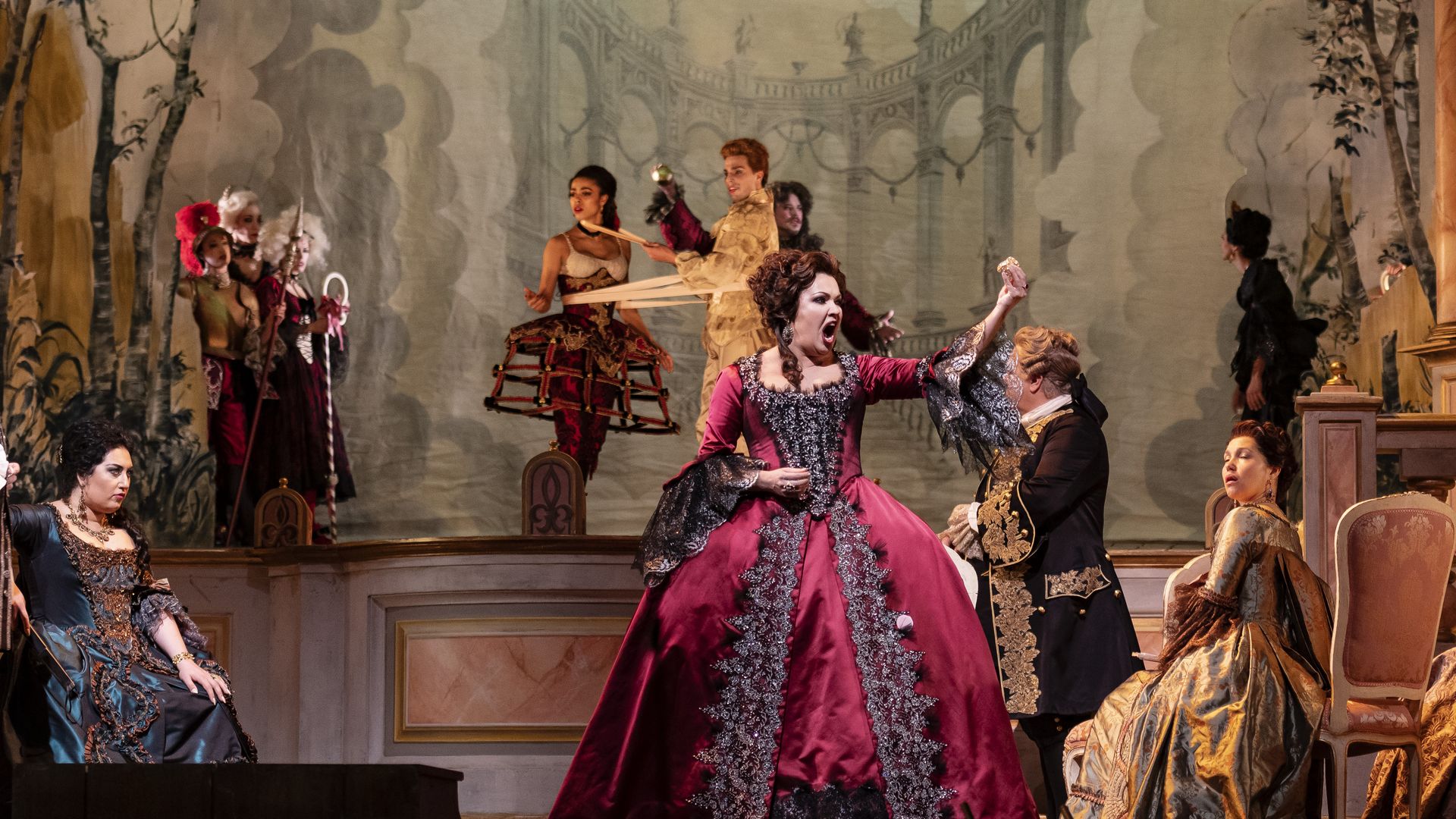 Photo of a woman dressed in finery raising one fist as she sings on stage