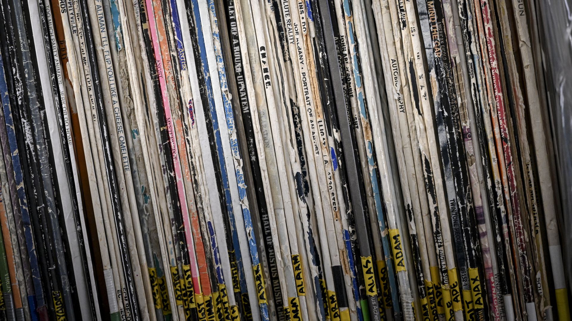 Close-up of a dense row of weathered magazine spines, colorful and worn, tightly packed with yellow tabs, creating a textured, tilted bookshelf look.