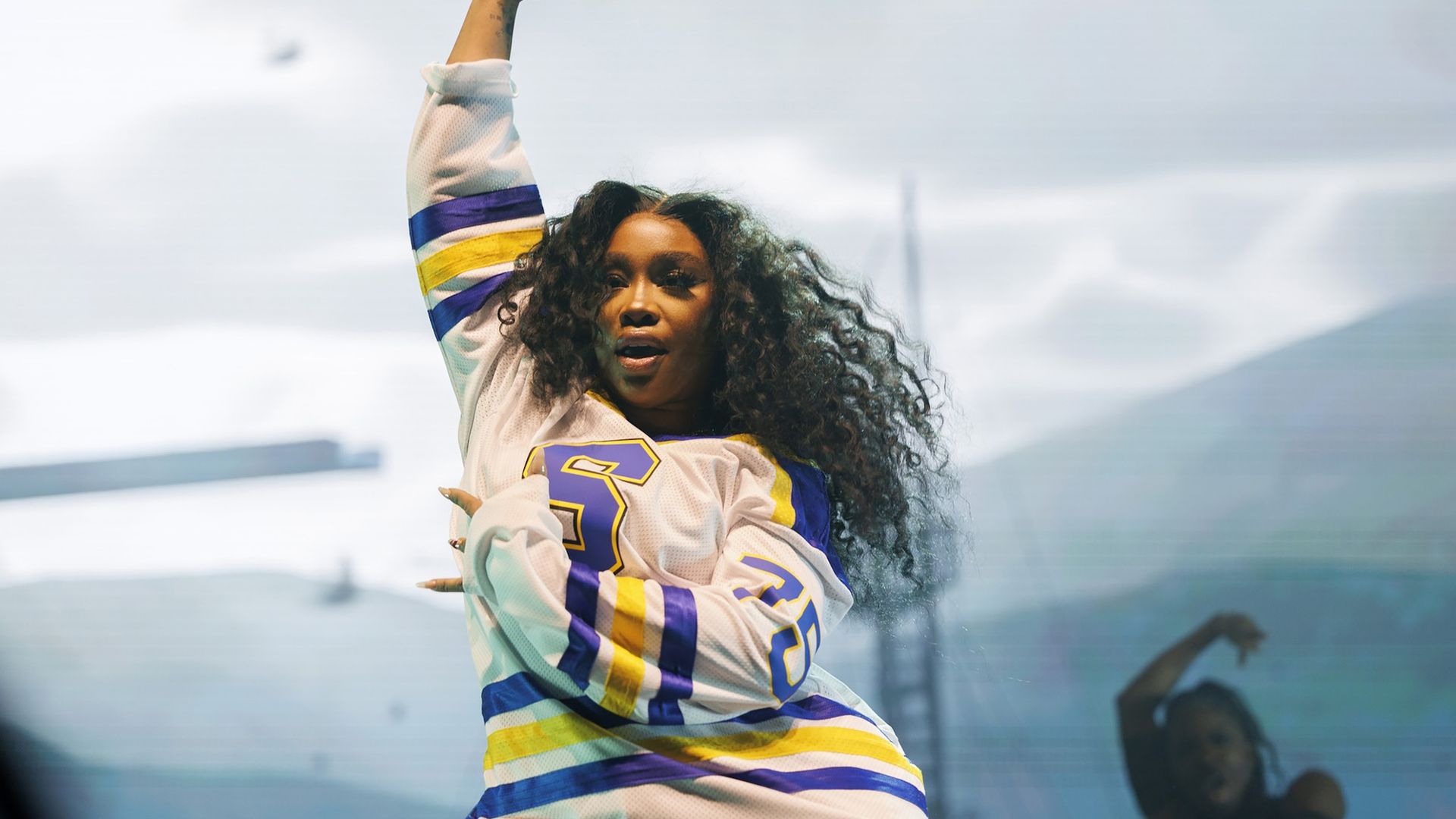 SZA performing with her arm in the air holding a microphone.