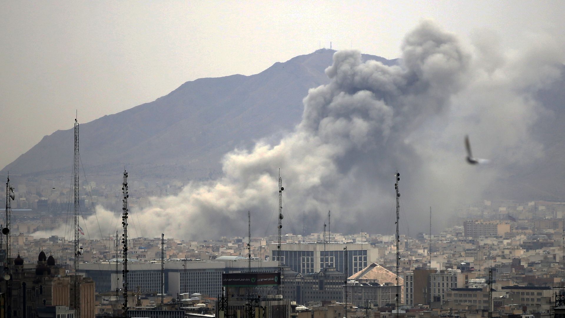 Smoke billows above Tehran buildings following airstrikes as part of a wider regional conflict.