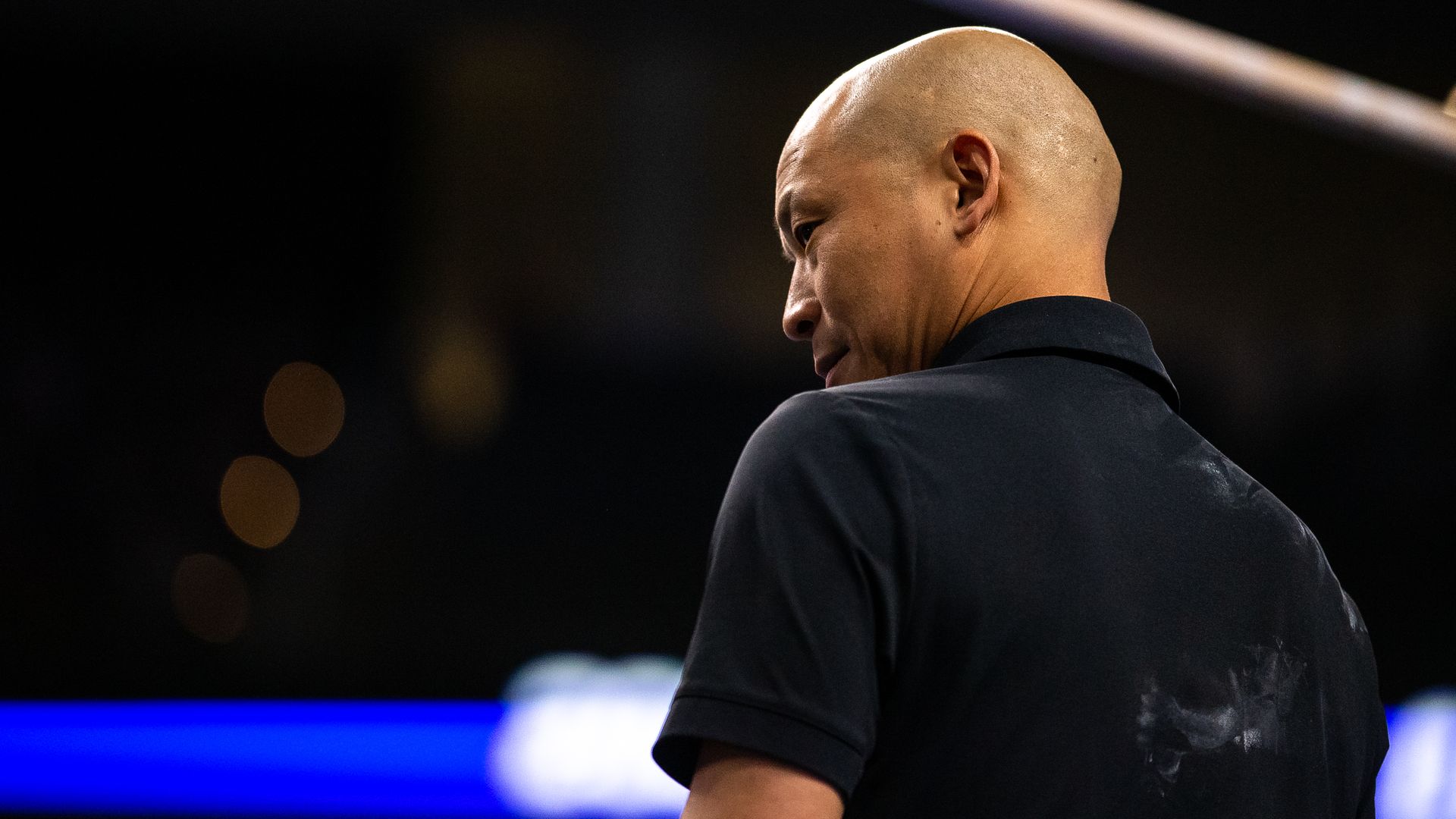 A man with a black polo shirt looks down.