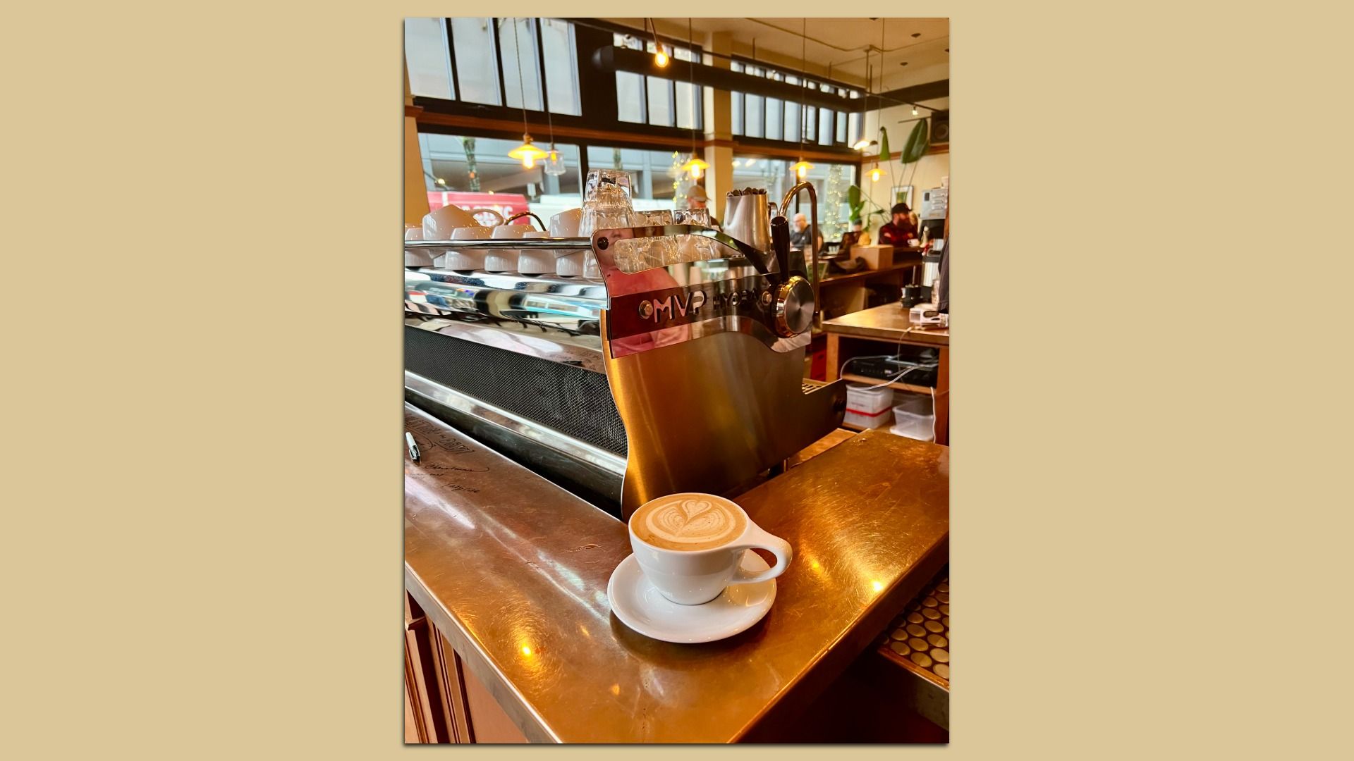 A latte in a mug sits on a copper counter in a coffee shop.