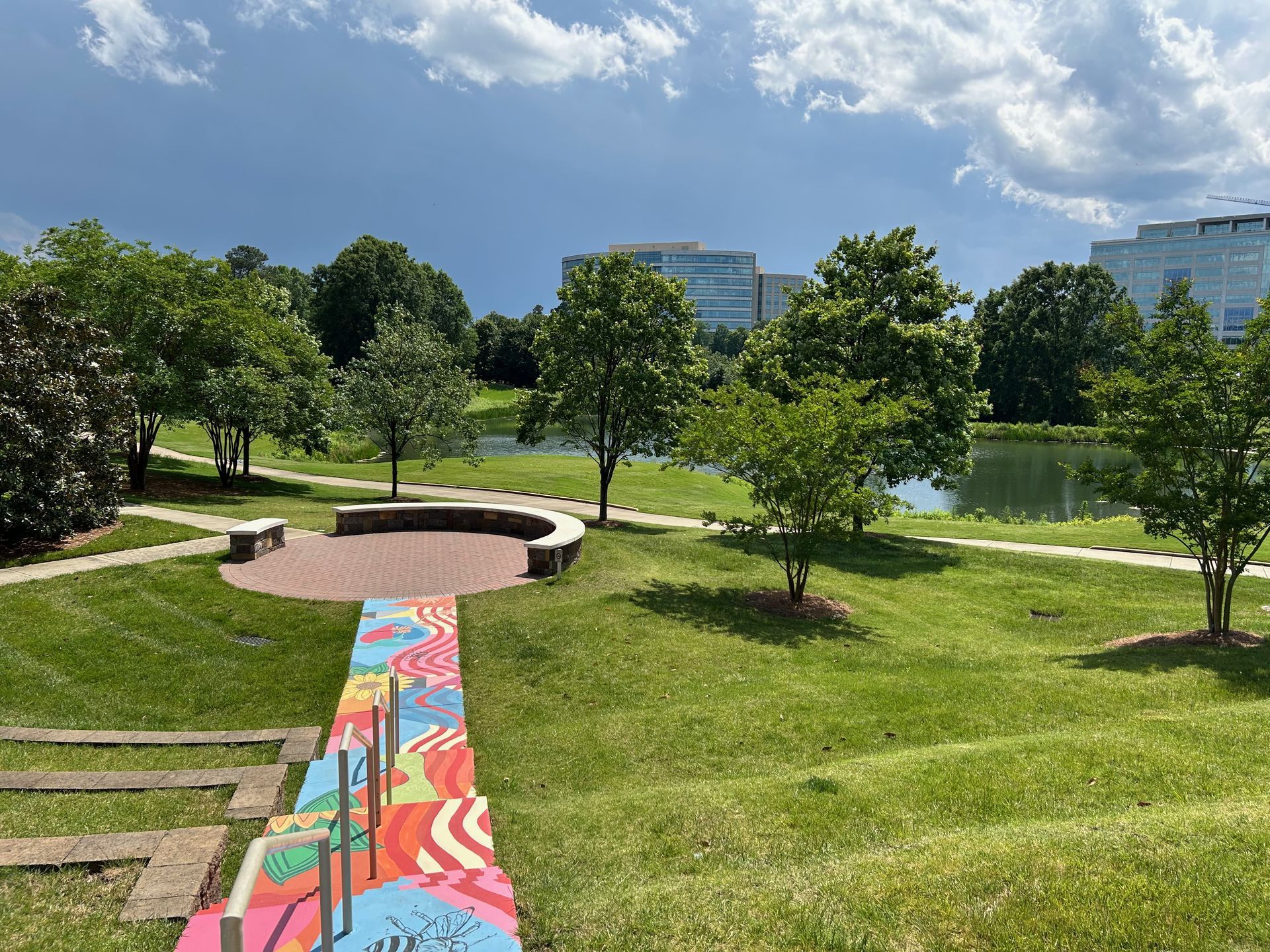 Rolling hills, painted steps and office buildings tower over trees. There's a pond in the distance. 