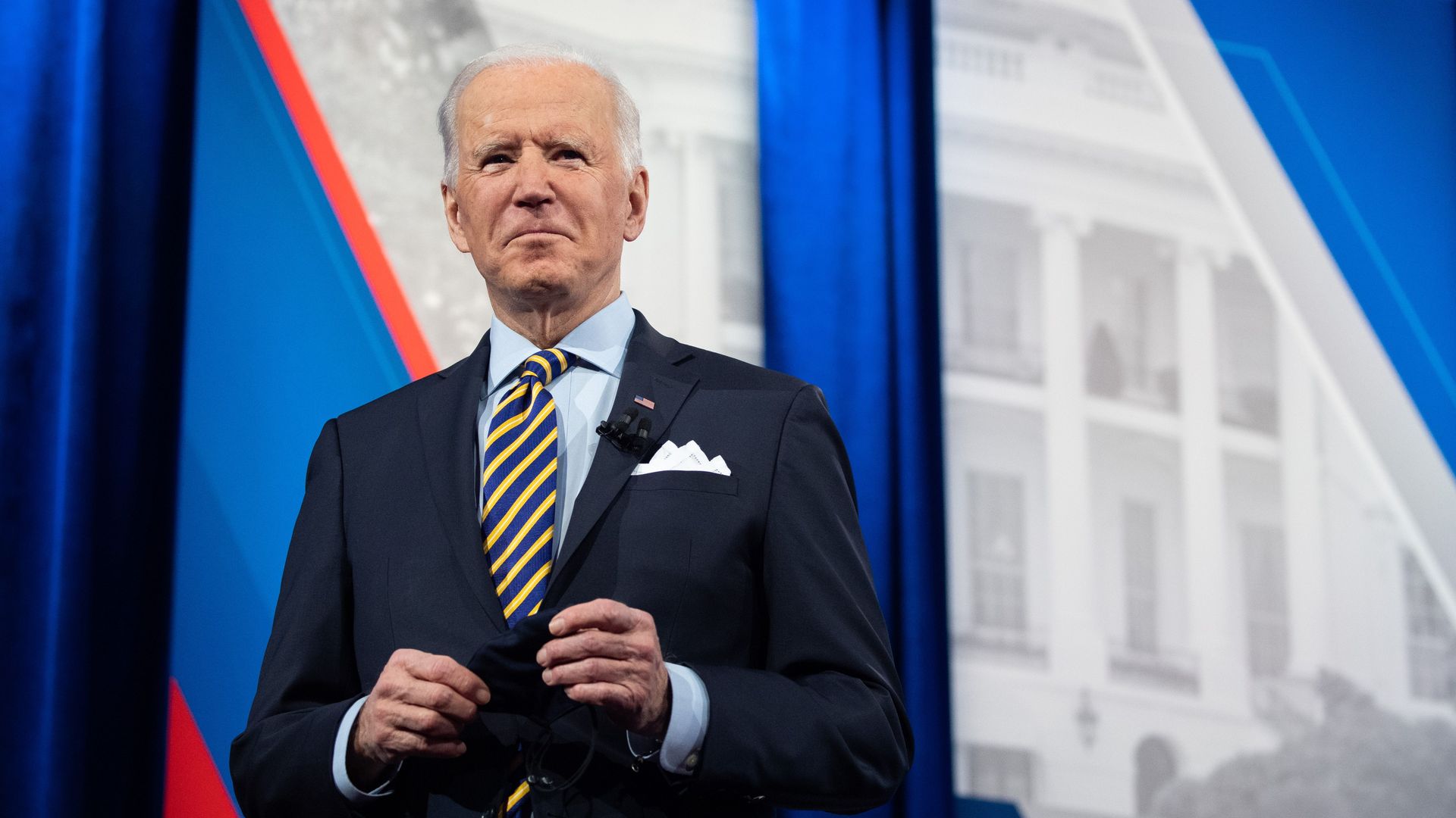 Joe Biden standing on a stage holding his face mask