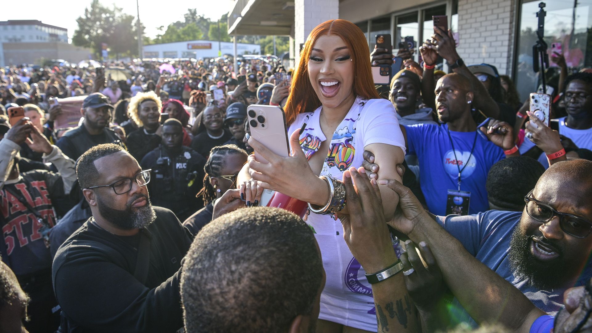 Cardi B holds a cell phone up to her face as a crowd of people surround her outside a store in metro Atlanta.
