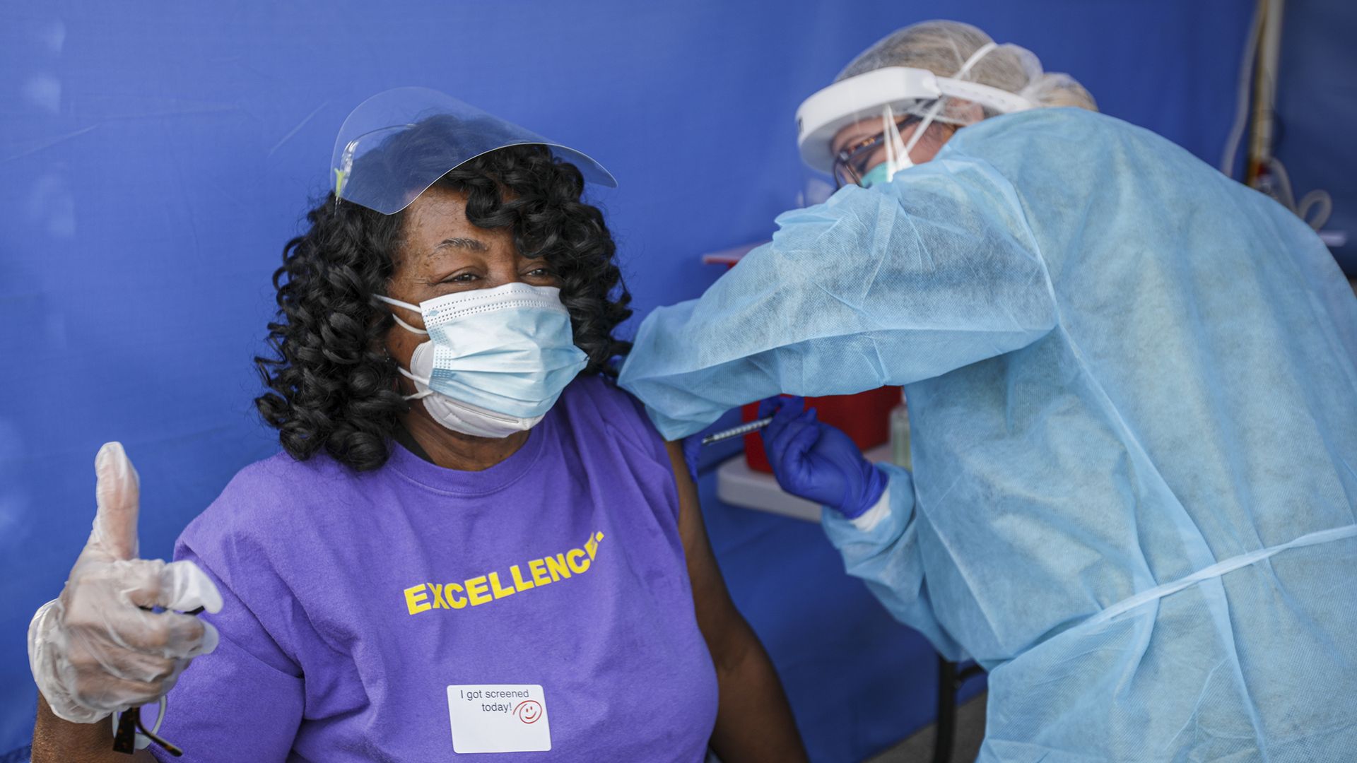 Healthcare worker Karen Crawford gives a thumbs up sign, left, as nurse Yolanda Javier administers a Pfizer-BioNTech COVID-19 vaccine in LA