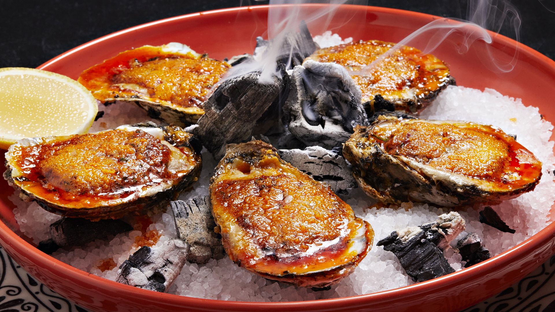 Grilled oysters on a platter with charcoal and lemon