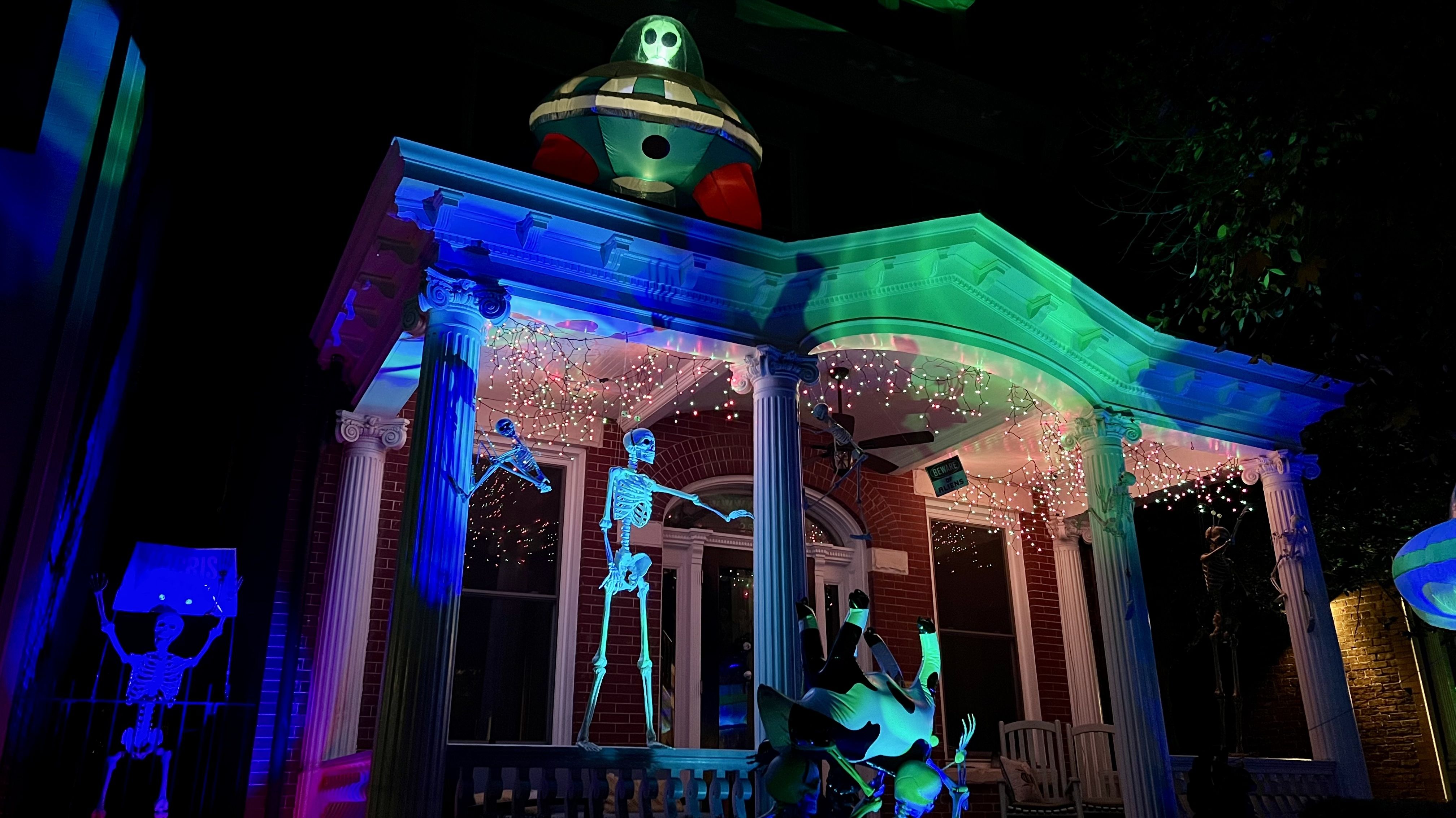 a pic of a house with a ufo and alien on top and skeletons carrying an inflatable cow