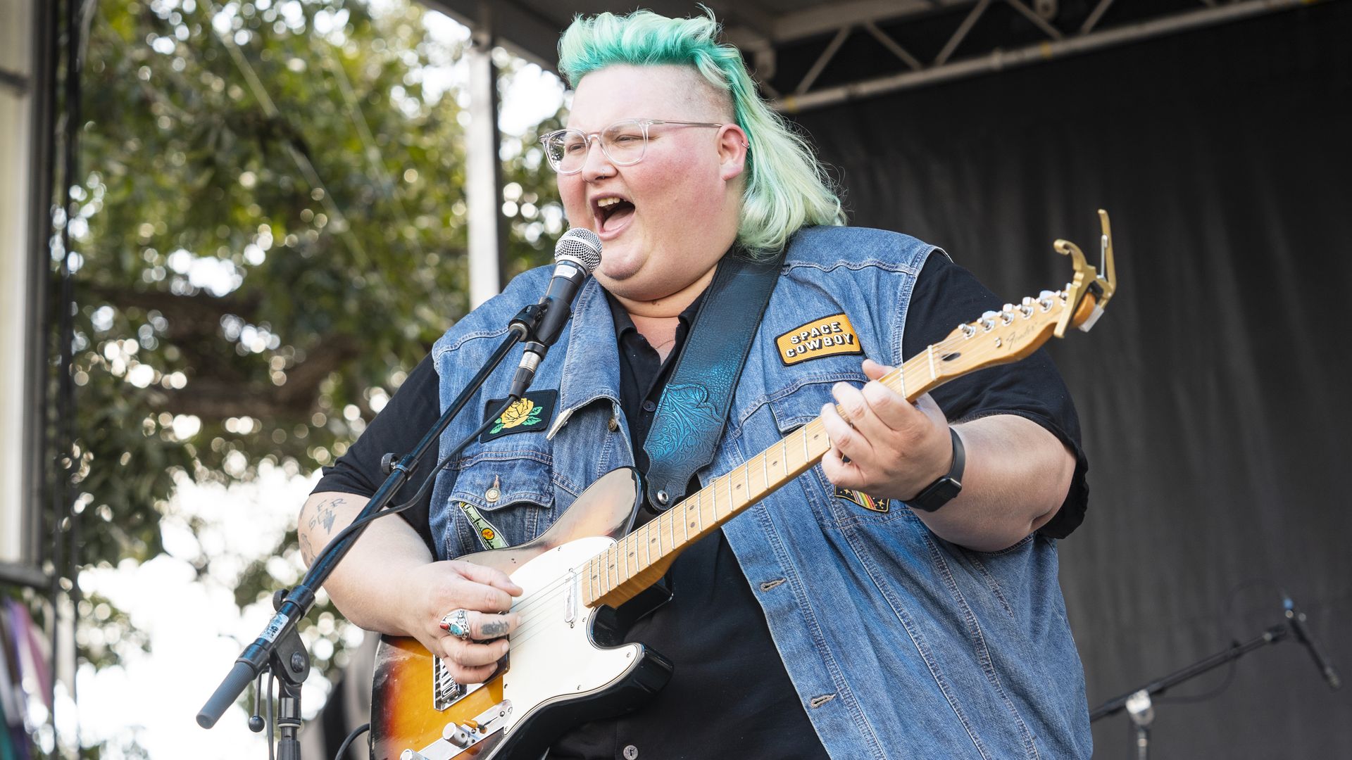 A green-haired musician rocks a guitar on stage