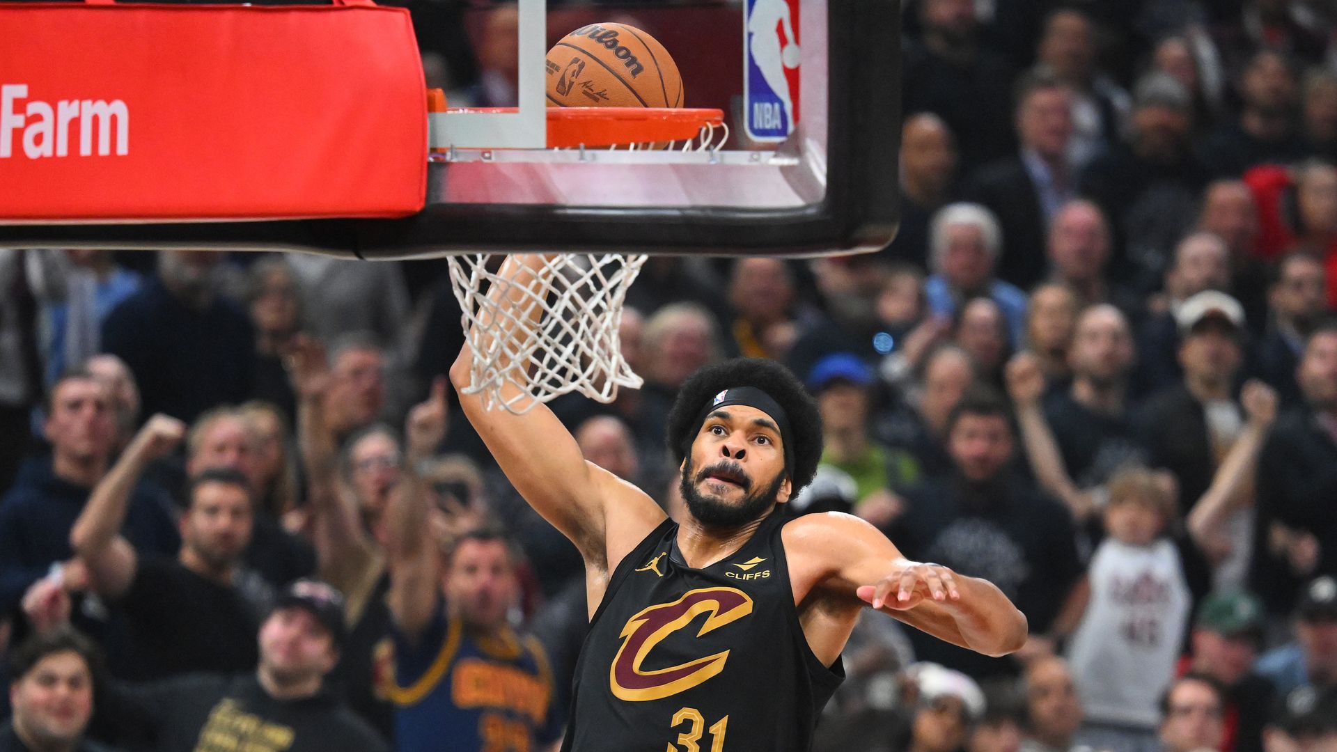 A basketball player in black jersey #31 with red "C" on front raises arm to slam basketball through hoop.