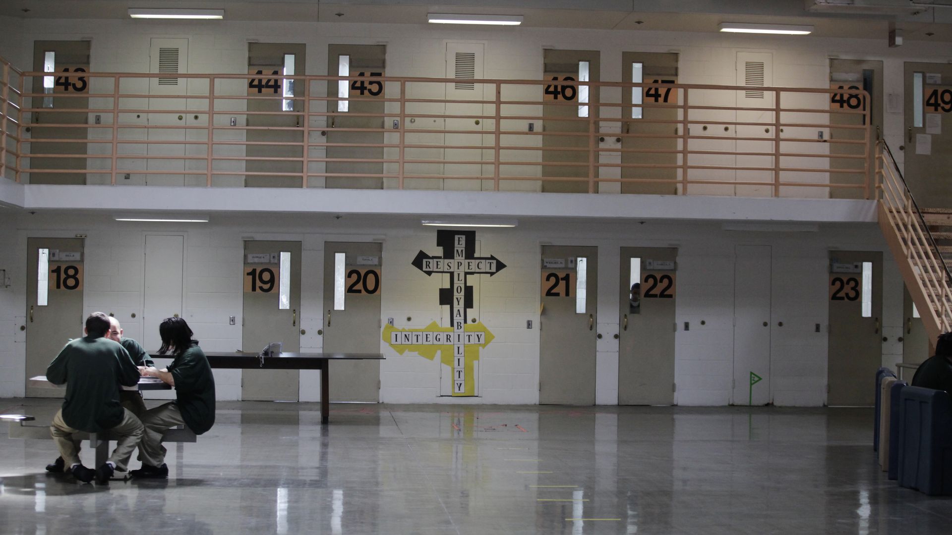 a California prison for youths. two people sit at a table. in the background, there are jail cells. 