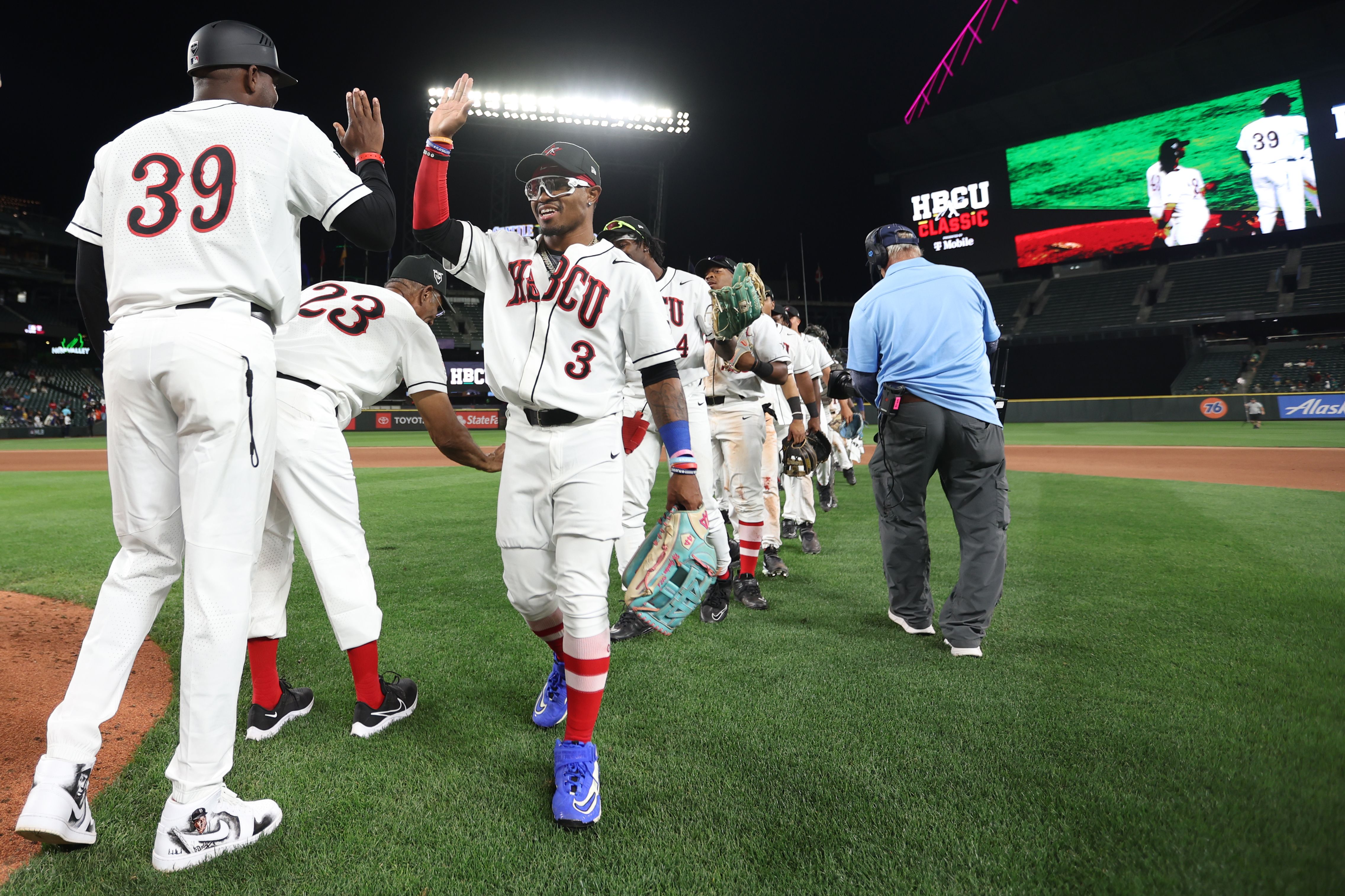 Players in white and red jerseys high five on the diamond during a night time game.